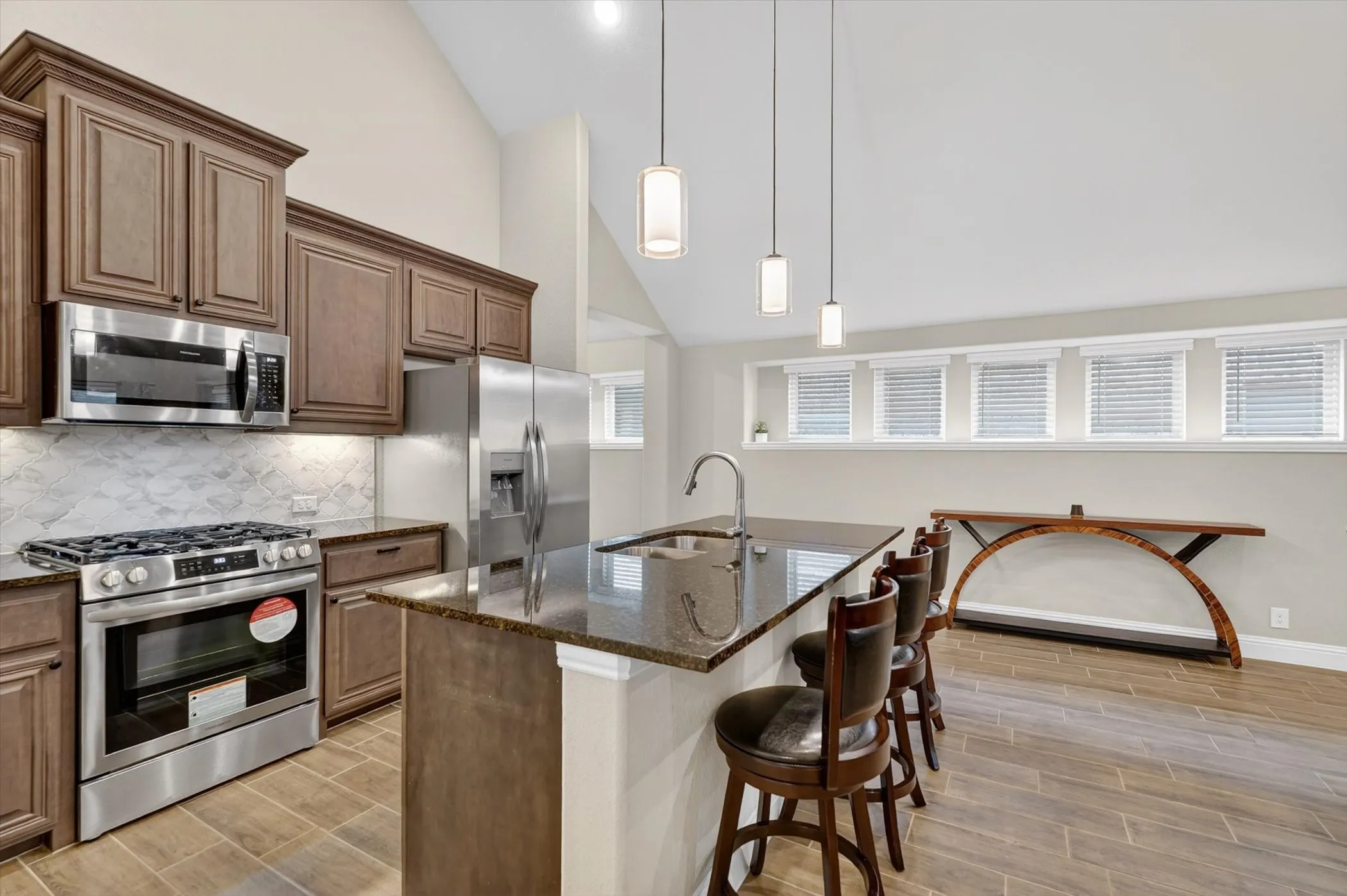 Kitchen featuring stainless steel appliances, dark wood cabinetry, and a central island with a sink and pendant lighting