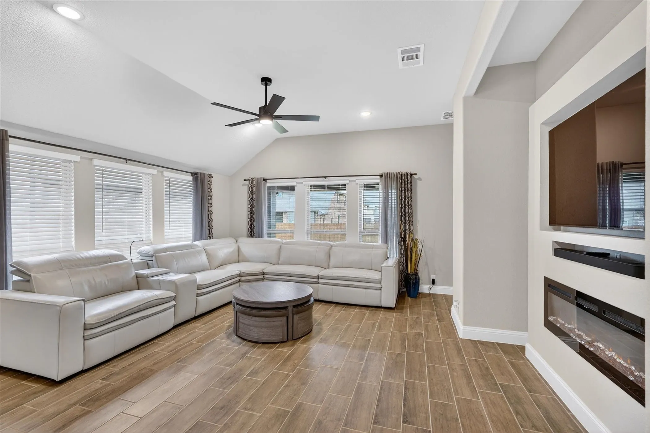 Vaulted ceiling with recessed lighting, wood-finish flooring, built-in media center, and multiple windows