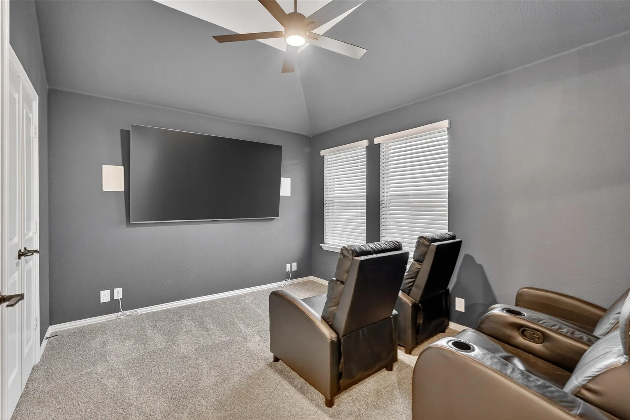 Vaulted ceiling with a ceiling fan, wall-mounted display, and two windows with blinds