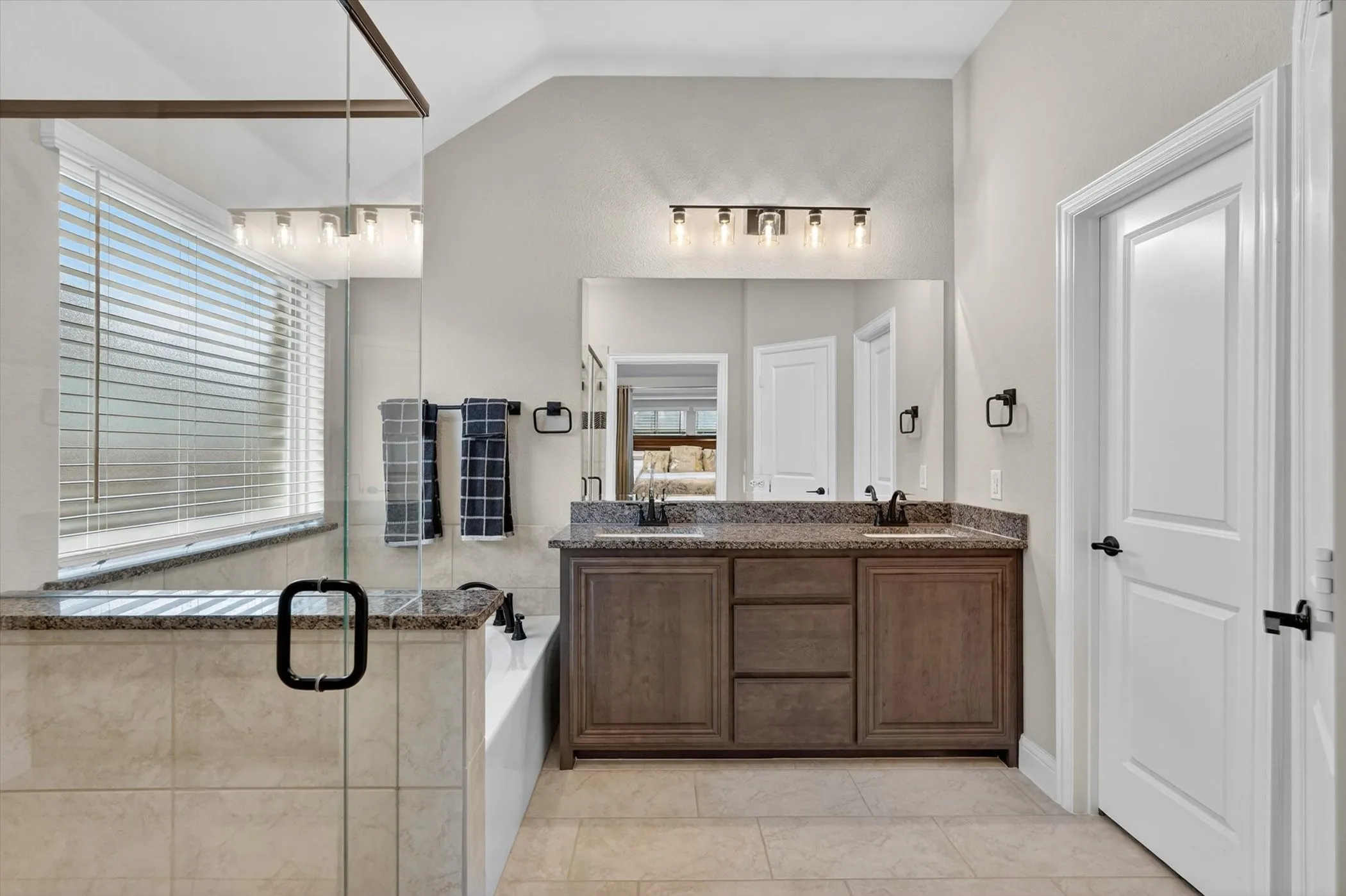 Dual vanity with stone countertops, wood-finish cabinetry, and matte black fixtures