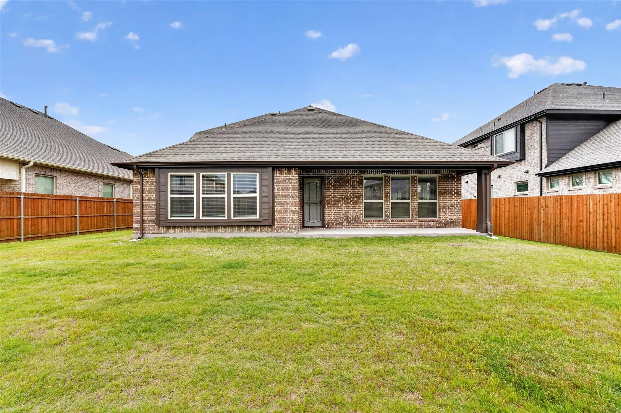 Brick exterior with a covered patio, multiple windows, and a privacy fence