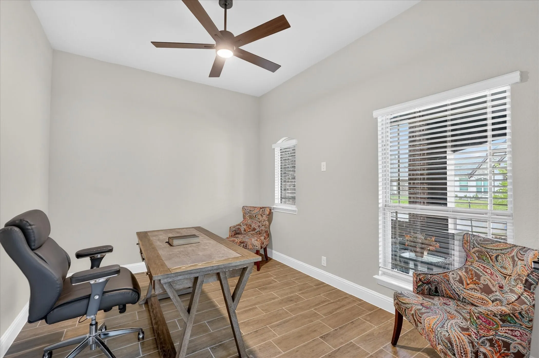 Vaulted ceiling featuring a ceiling fan with integrated lighting, wood-finish flooring, and multiple windows with blinds