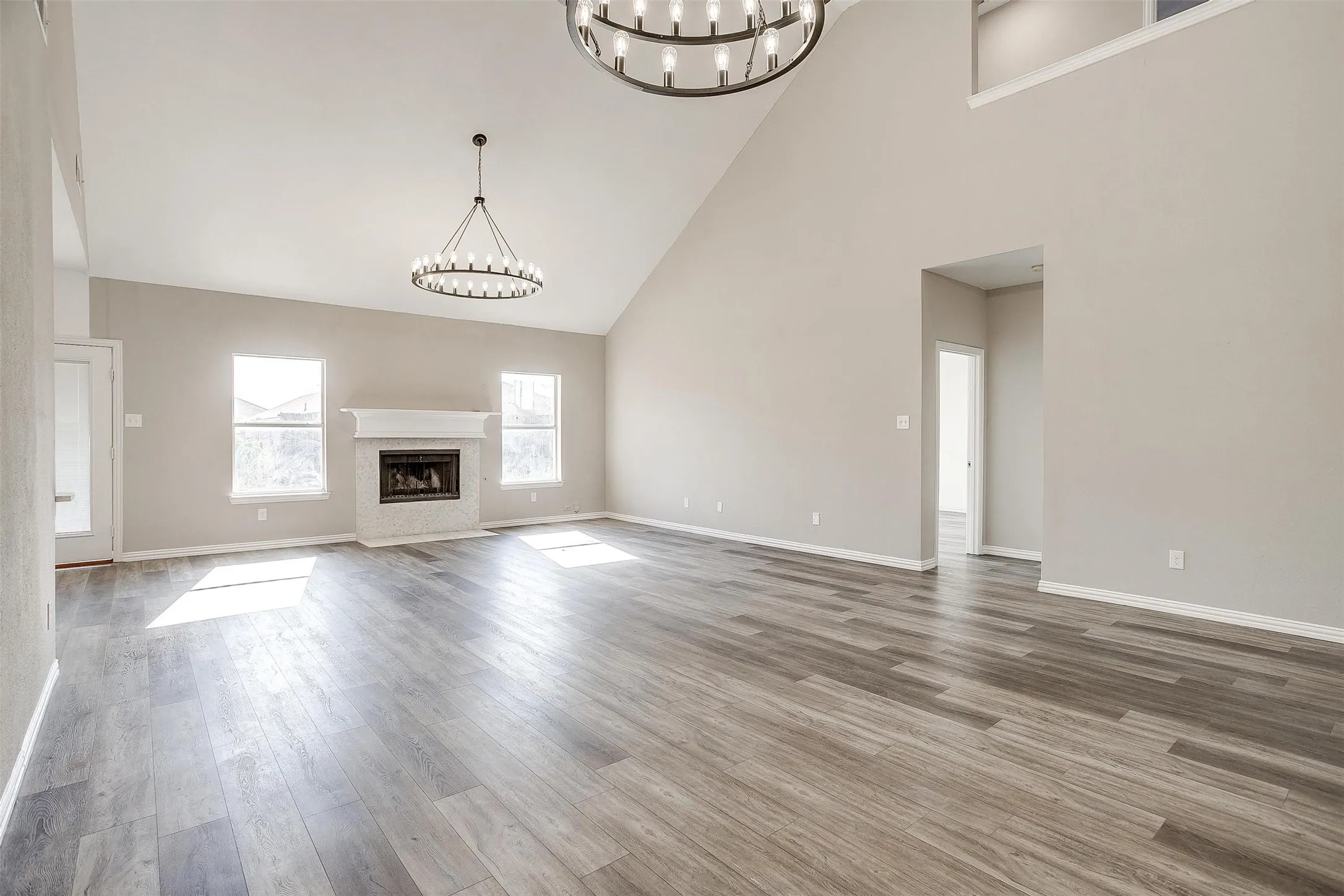 Spacious living area featuring high vaulted ceilings, wood-finish flooring, and a fireplace with a white mantel and tile surround