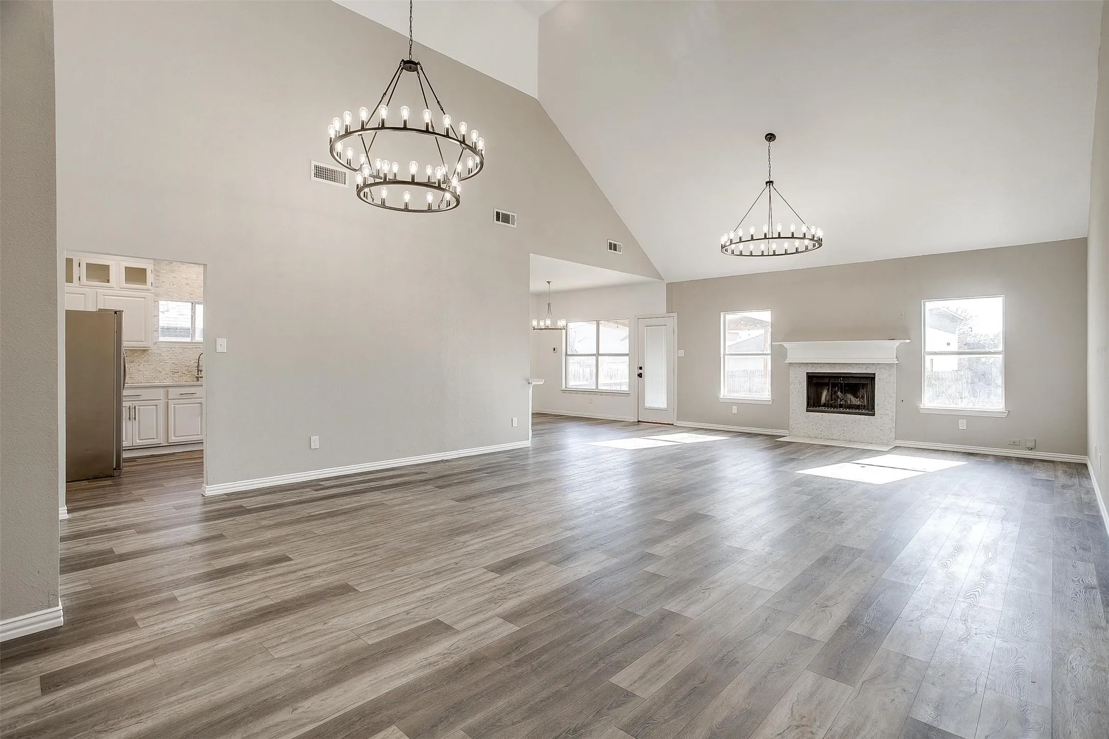 Vaulted ceilings with contemporary chandeliers, wood-finish flooring, and a fireplace with a white mantel