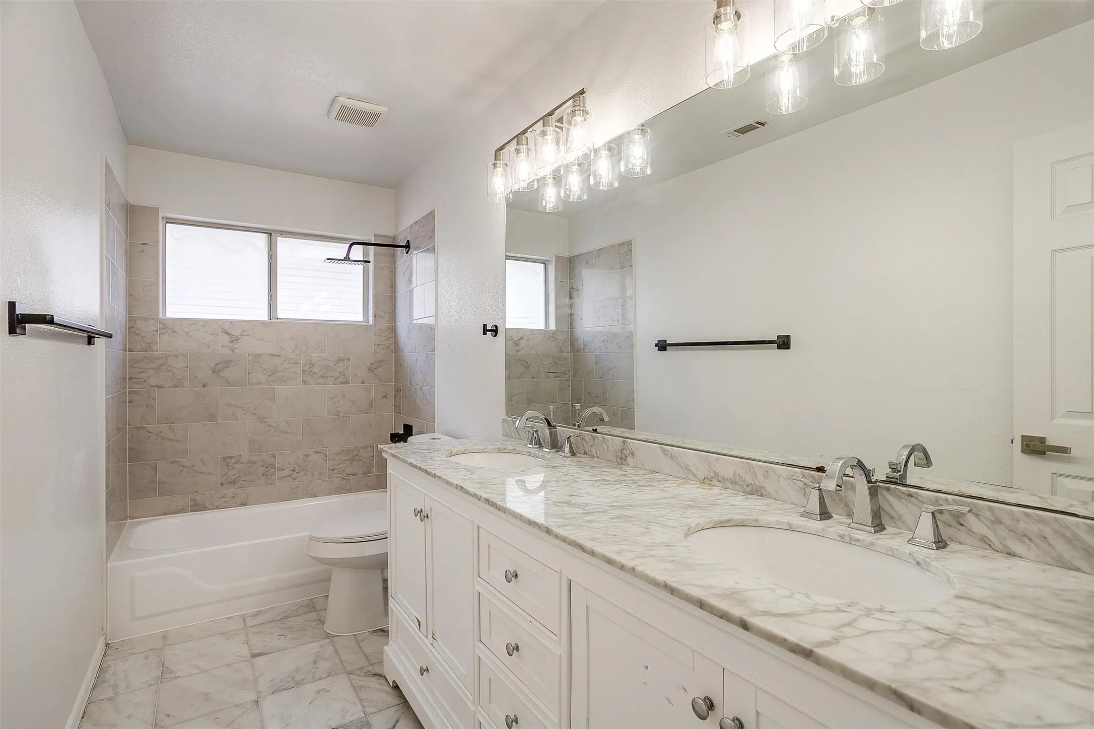 Spa-inspired primary bathroom featuring a dual-sink vanity with marble-finish countertop and polished nickel faucets, frameless glass-enclosed shower with tile surround, soaking tub, and polished stone flooring