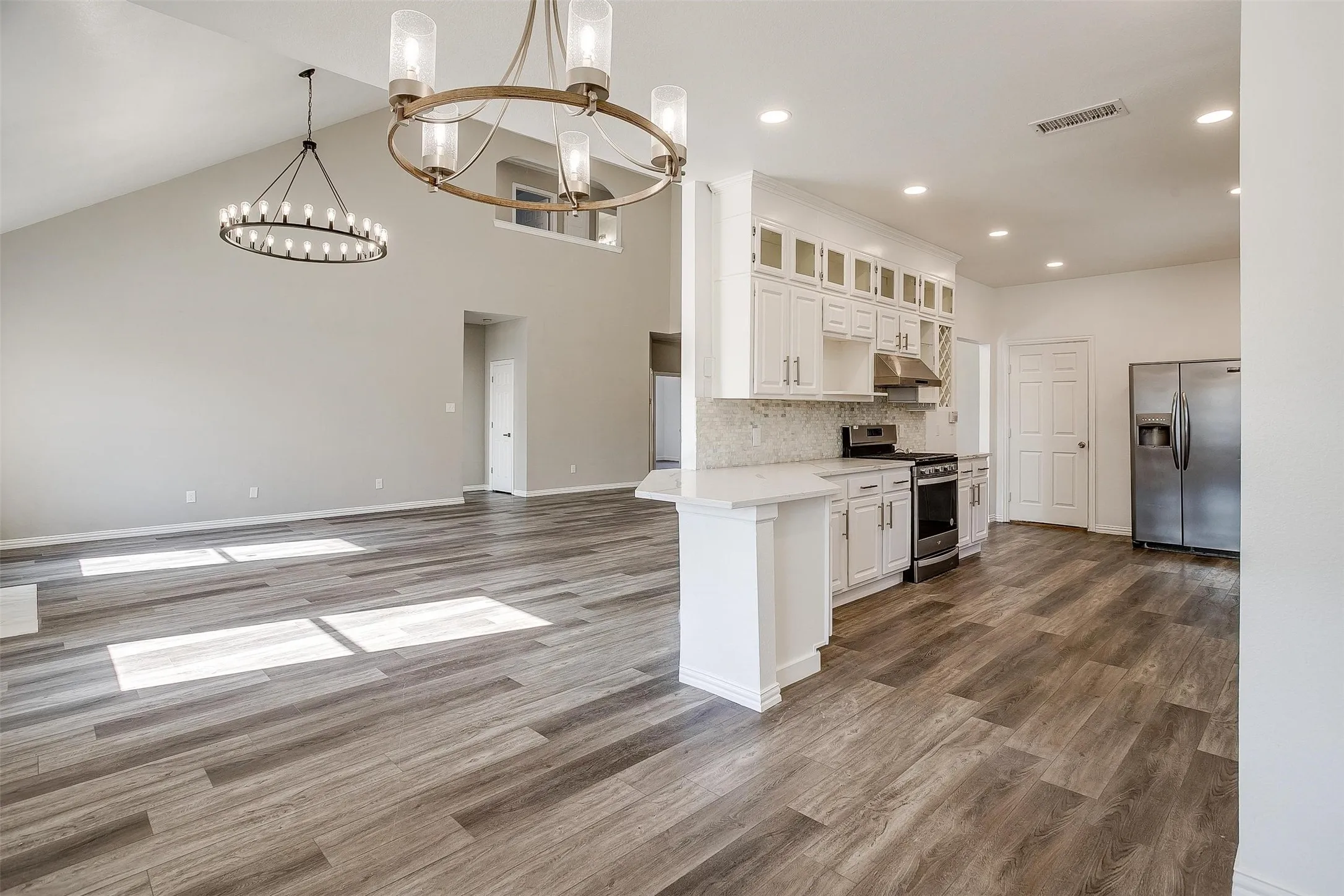 Open-concept living space featuring vaulted ceilings, wood-finish flooring, a kitchen with white cabinetry, stainless steel appliances, and a breakfast bar