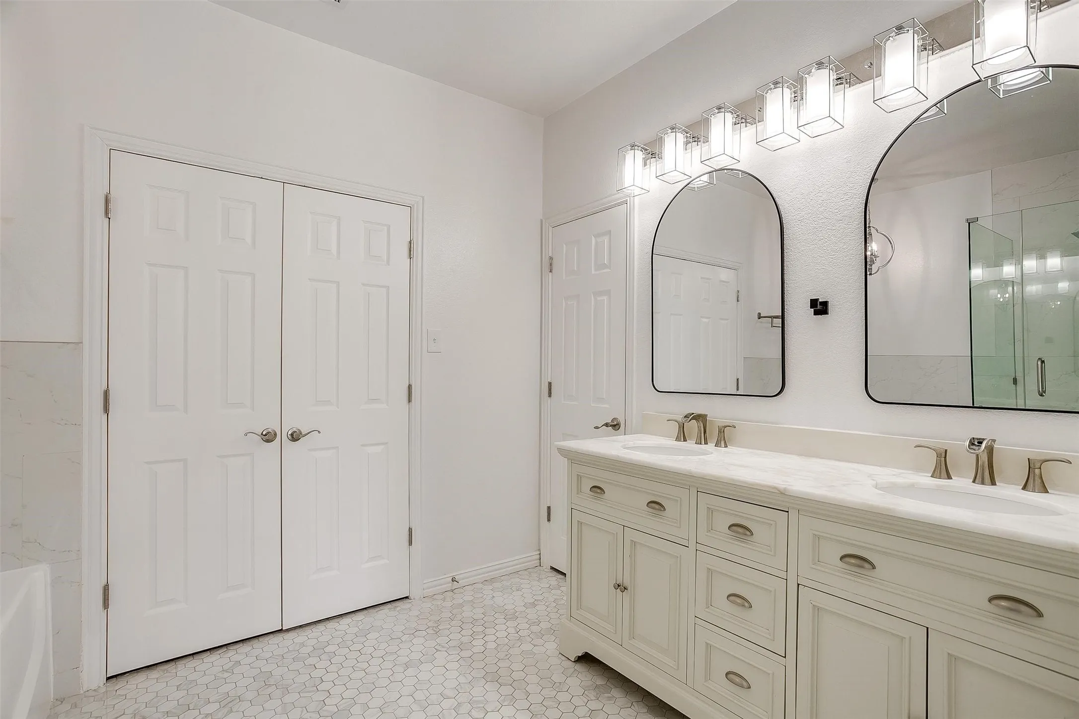 Spa-inspired primary bathroom featuring dual vanities with cream cabinetry, brushed nickel hardware, and an extended countertop with integrated sink