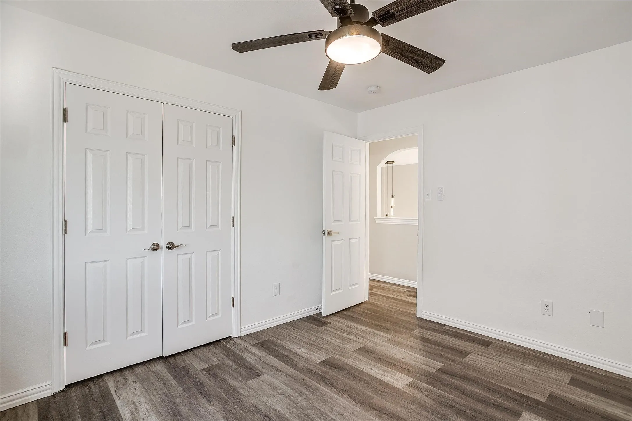Wood-finish flooring, white paneled doors, ceiling fan with integrated lighting, and white wall finishes