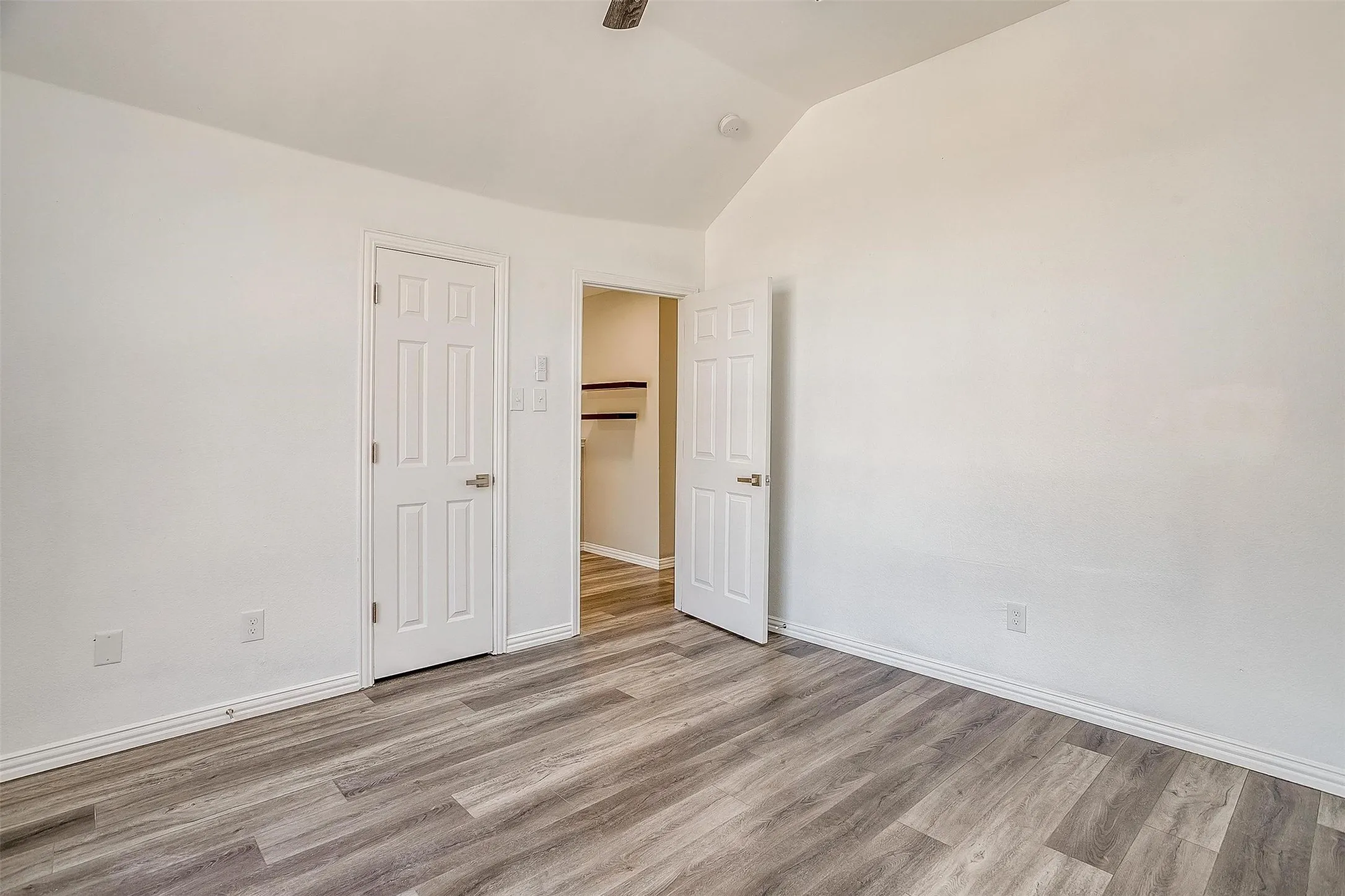 Vaulted ceiling, wood-finish flooring, white paneled doors, and ceiling fan