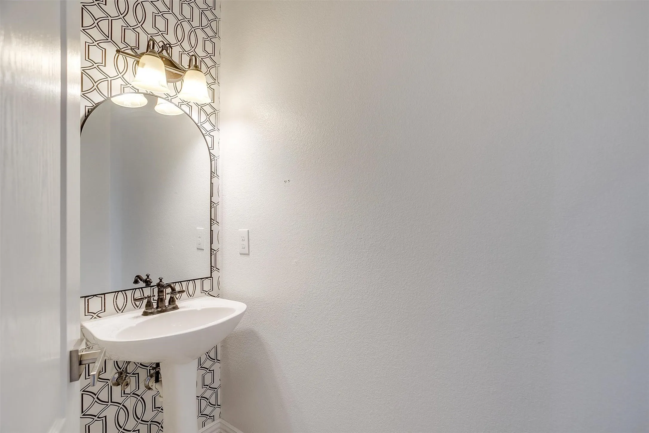 Pedestal sink with a decorative faucet, an arched mirror, and a three-light vanity fixture