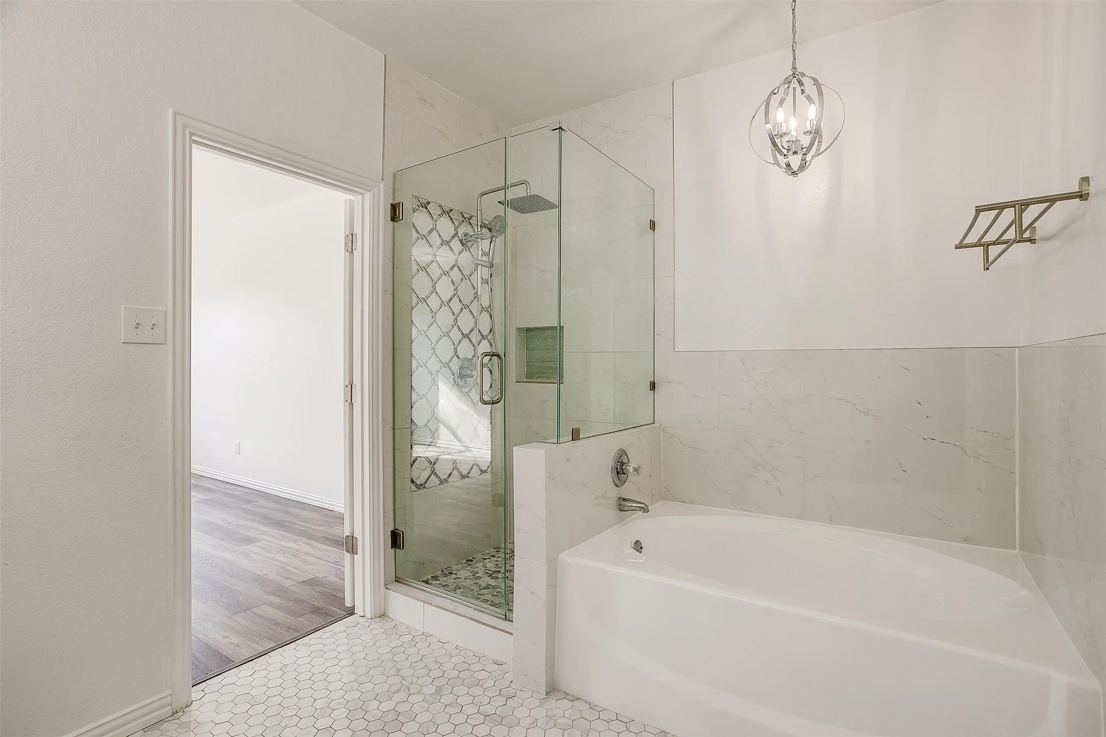 Spa-inspired primary bathroom featuring a freestanding soaking tub, frameless glass-enclosed shower with mosaic tile accent wall, dual vanity with vessel sink, polished nickel fixtures, and hexagonal marble floor tile throughout