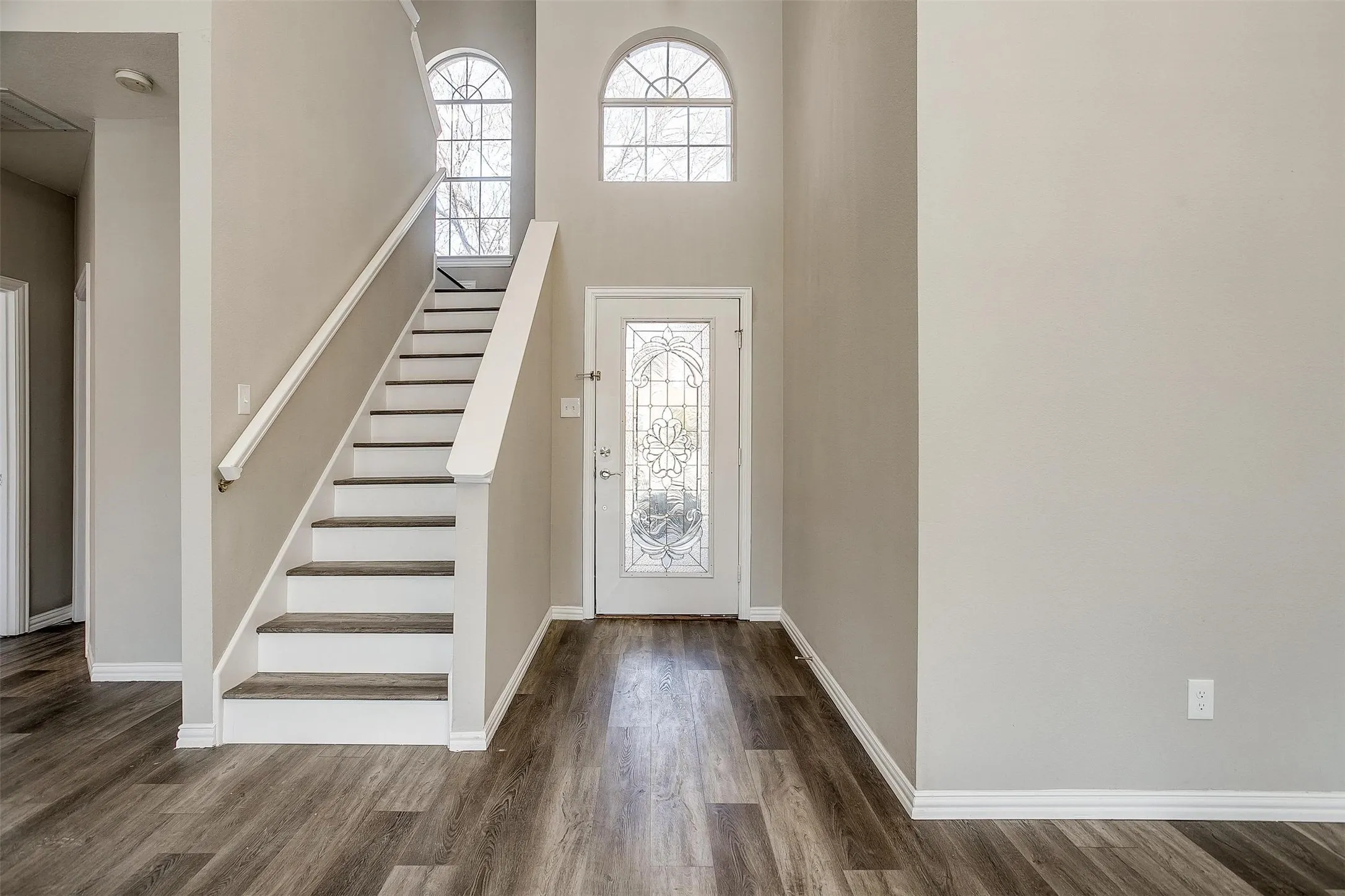 Foyer featuring wood-finish flooring, a staircase with white risers, and a front entry door with decorative glass