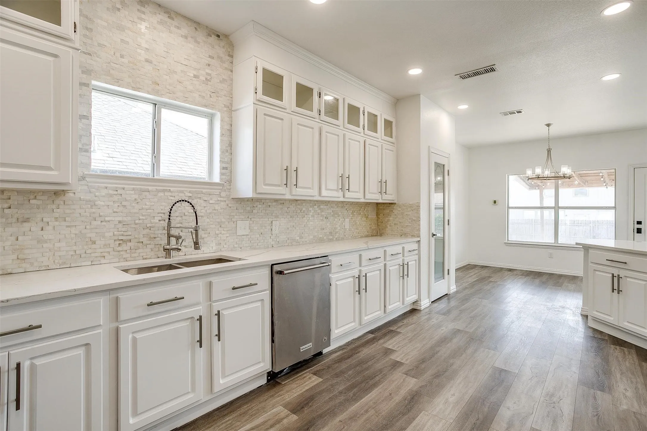 Kitchen featuring white cabinetry, light-toned stacked stone backsplash, stainless steel appliances, and wood-finish flooring