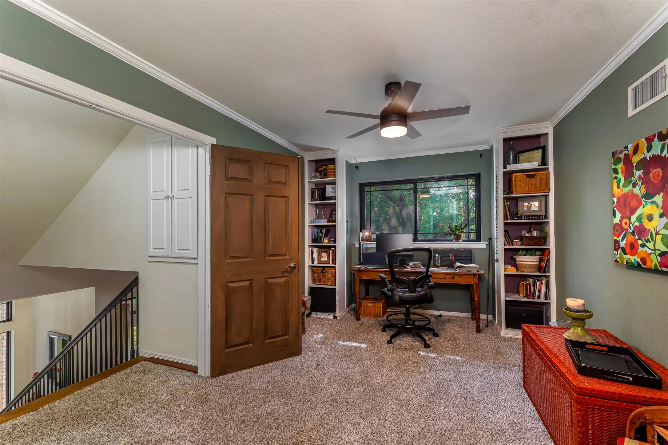 Built-in shelving units, ceiling fan, wood-paneled door, and carpeted flooring