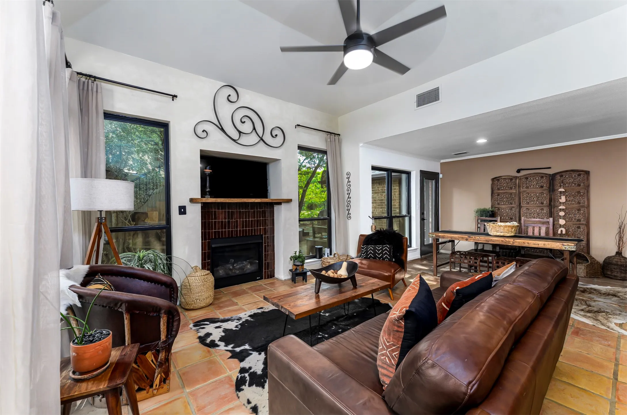 Sophisticated living room showcasing hardwood flooring, a linear fireplace with decorative mantelware, ceiling fan with integrated lighting, and expansive windows framed by floor-to-ceiling drapery