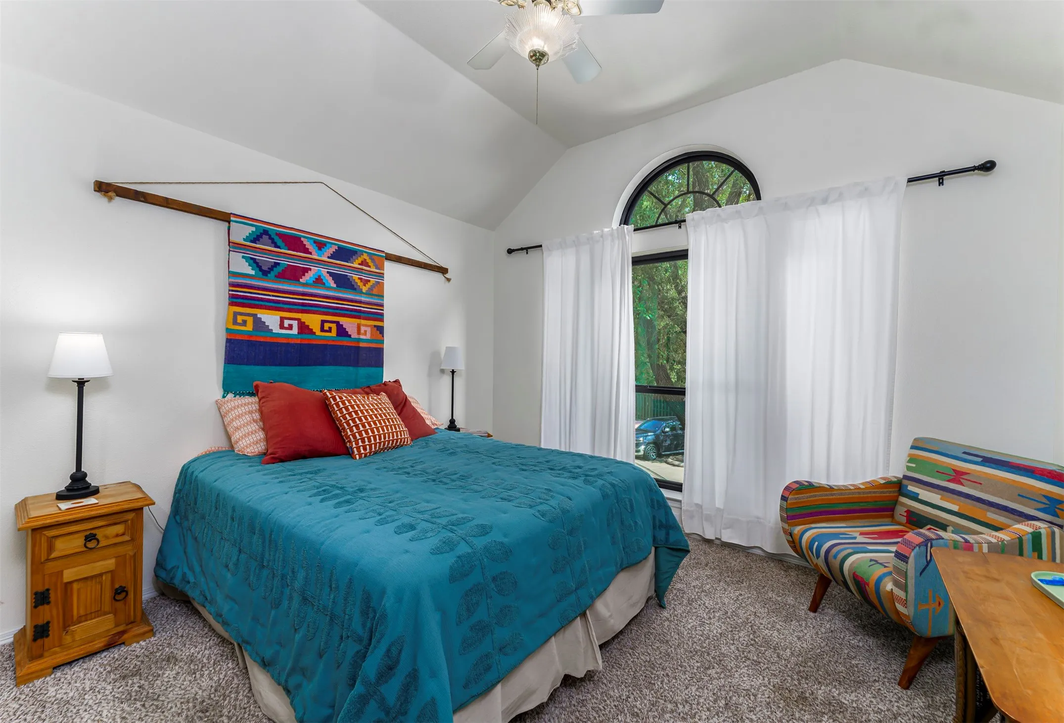 Vaulted ceiling with ceiling fan, arched window, and plush carpeting