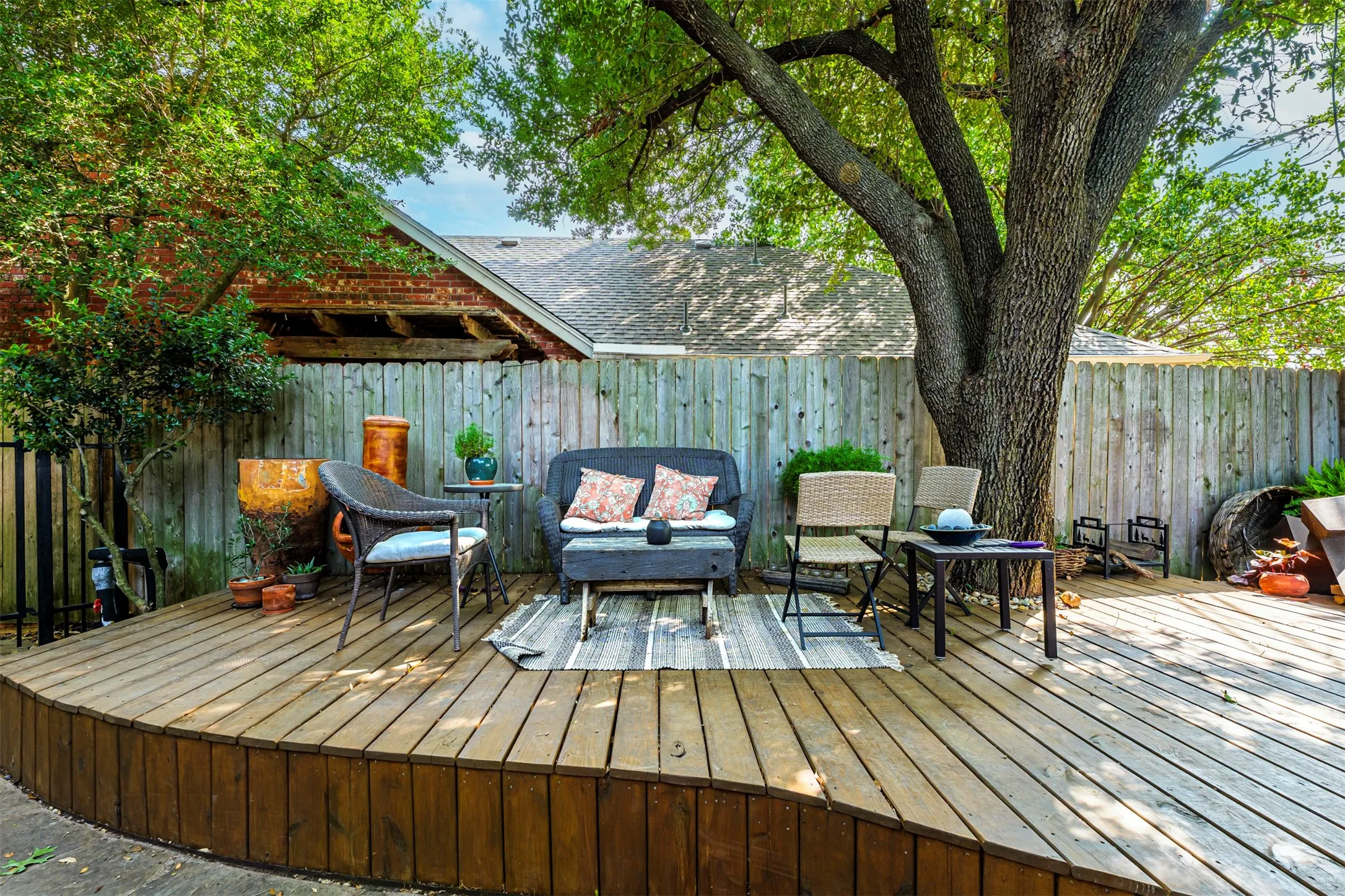 Expansive composite deck with wood-finish flooring and curved architectural detailing, anchored by a mature shade tree