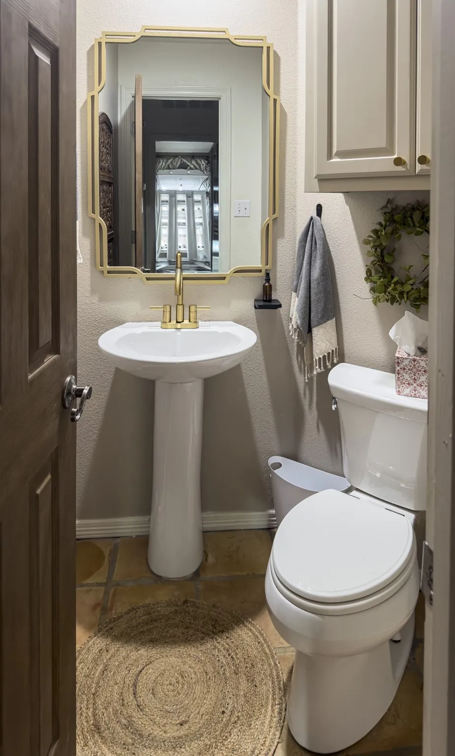 Pedestal sink with gold-tone fixtures, wall-mounted mirror, built-in cabinetry, and tile flooring