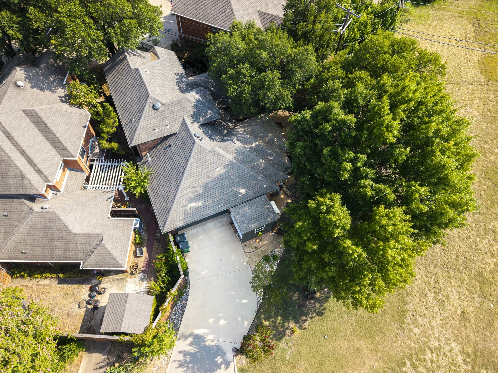 Asphalt shingle roofing, attached pergola structure, paved driveway, mature landscaping, and adjacent open greenspace