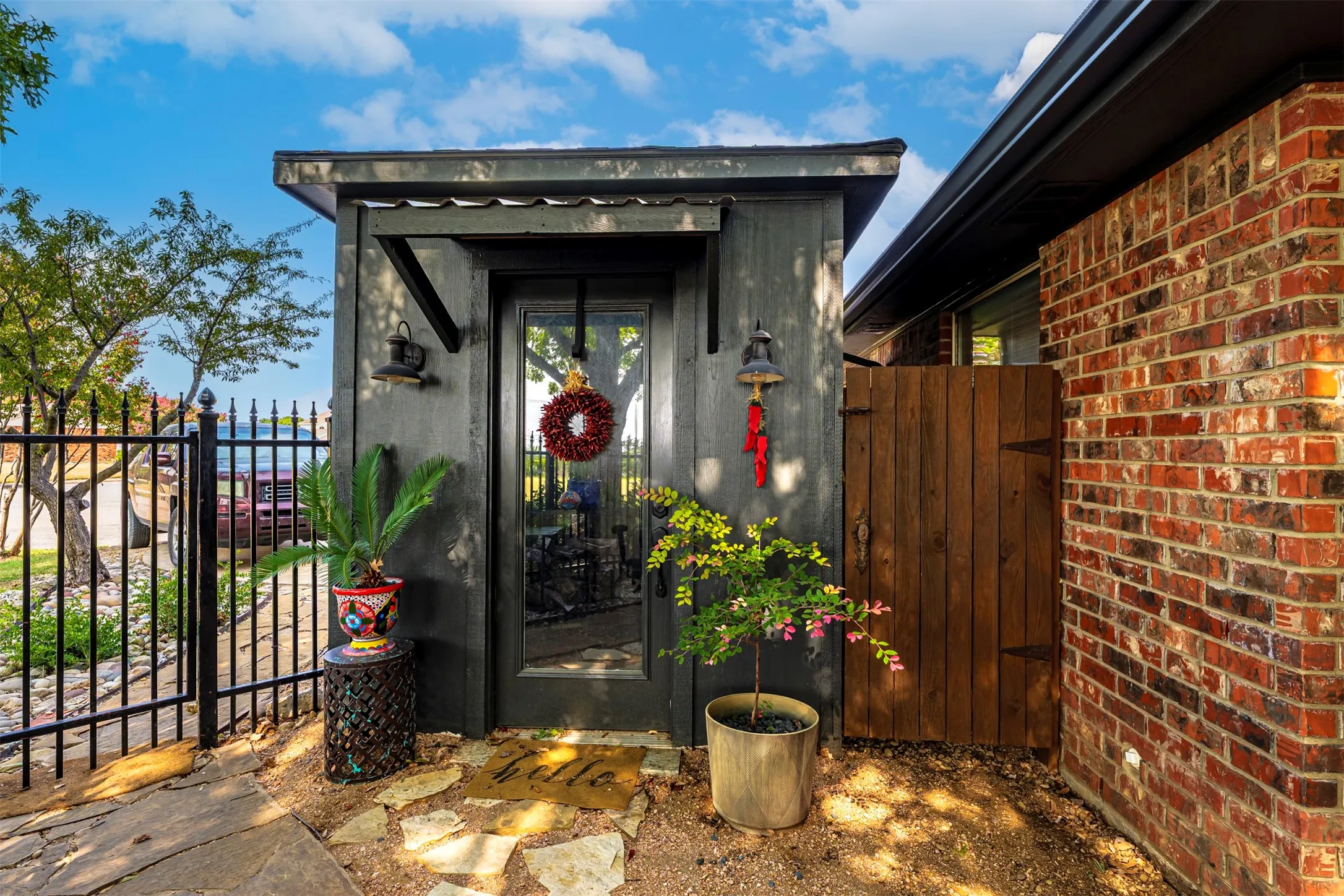 Dark-toned exterior structure with a glass-paneled entry door, wood privacy gate, and a black wrought iron fence