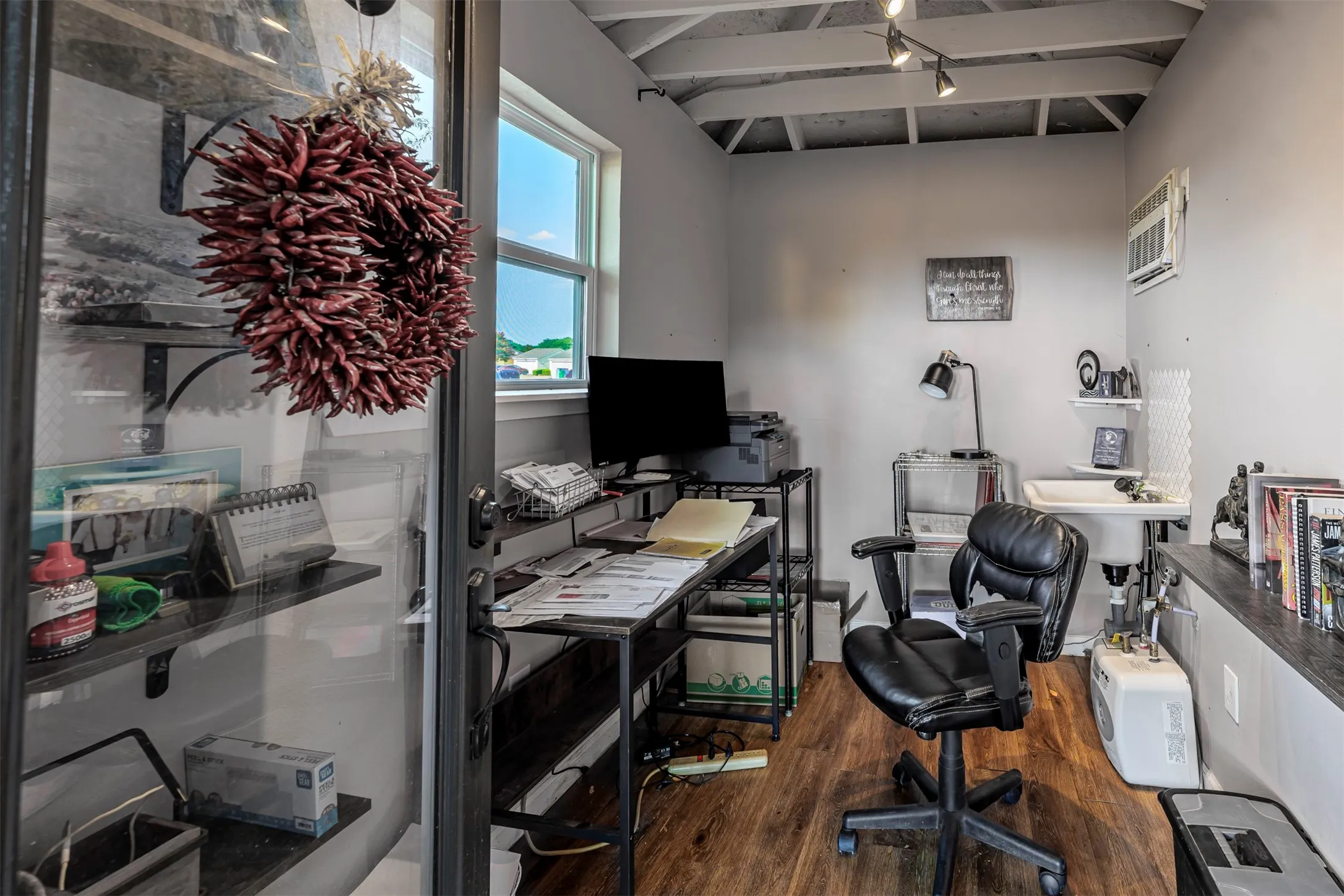 Compact interior space featuring wood-finish flooring, a window-mounted air conditioning unit, track lighting, and a utility sink