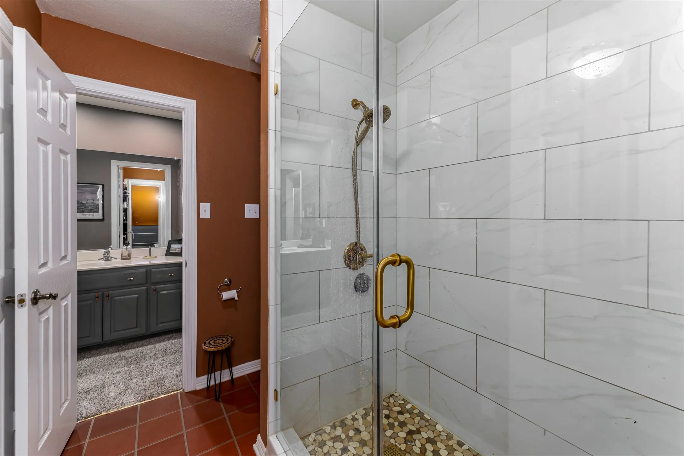Glass-enclosed shower with white subway tile surround, pebble tile floor, and brass-finish fixtures