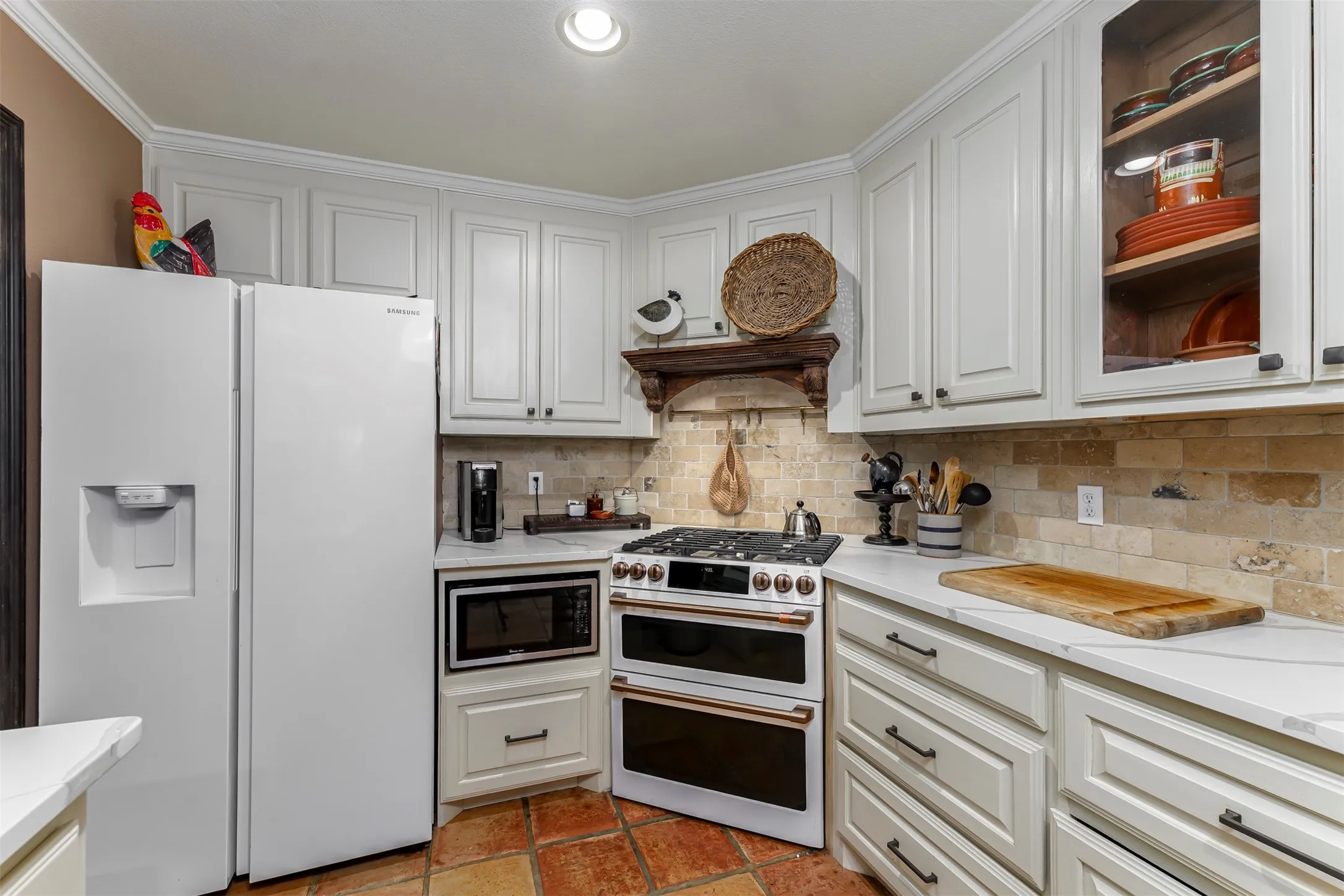 White cabinetry with dark hardware, stone tile backsplash, white countertops, built-in microwave, and tile flooring
