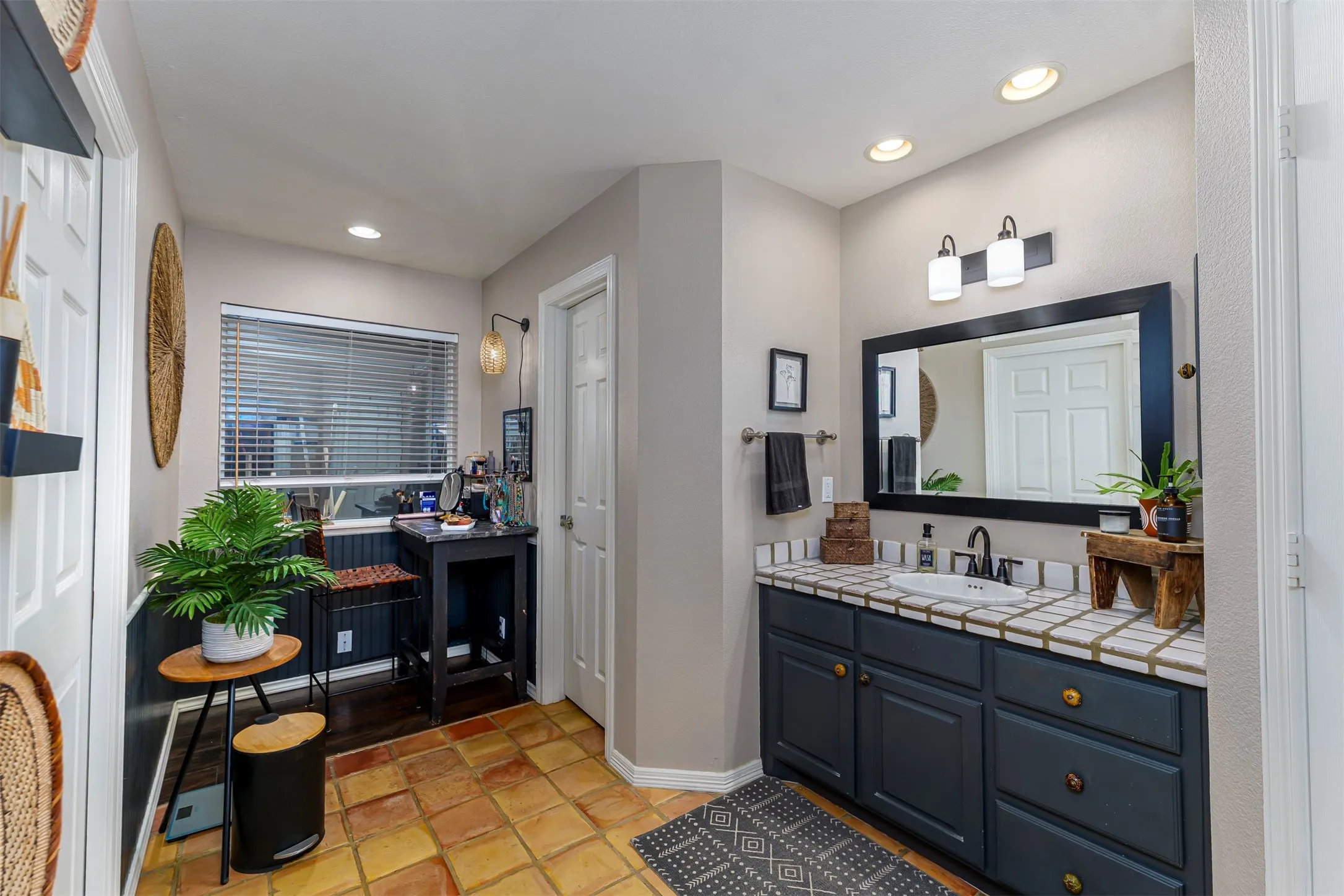 Bathroom featuring terra cotta tile flooring, a dark wood-finish vanity with a tile countertop, recessed lighting, and a window with blinds