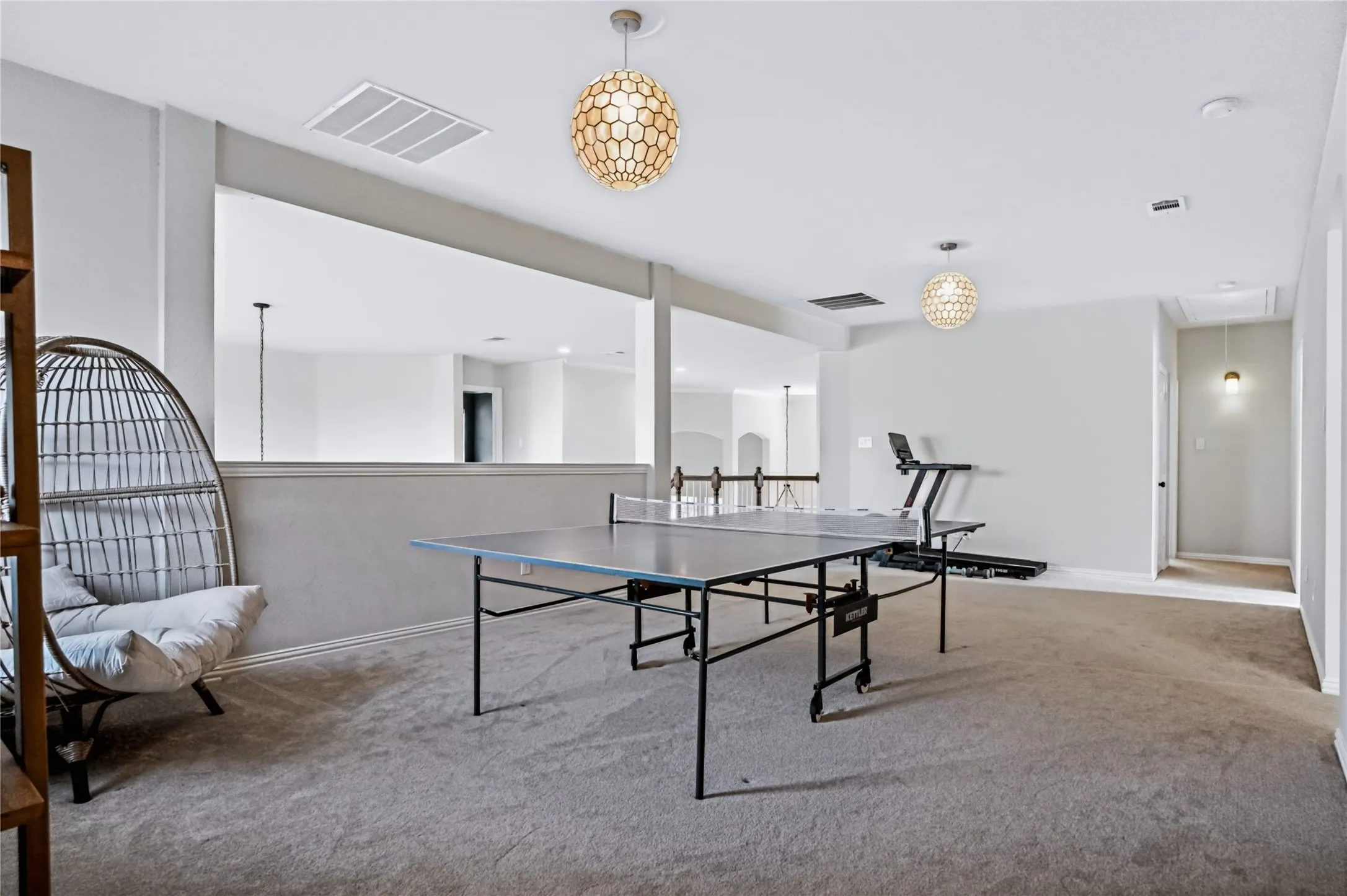 Carpeted open-concept bonus room featuring two decorative pendant lights and a half-wall overlooking a lower level