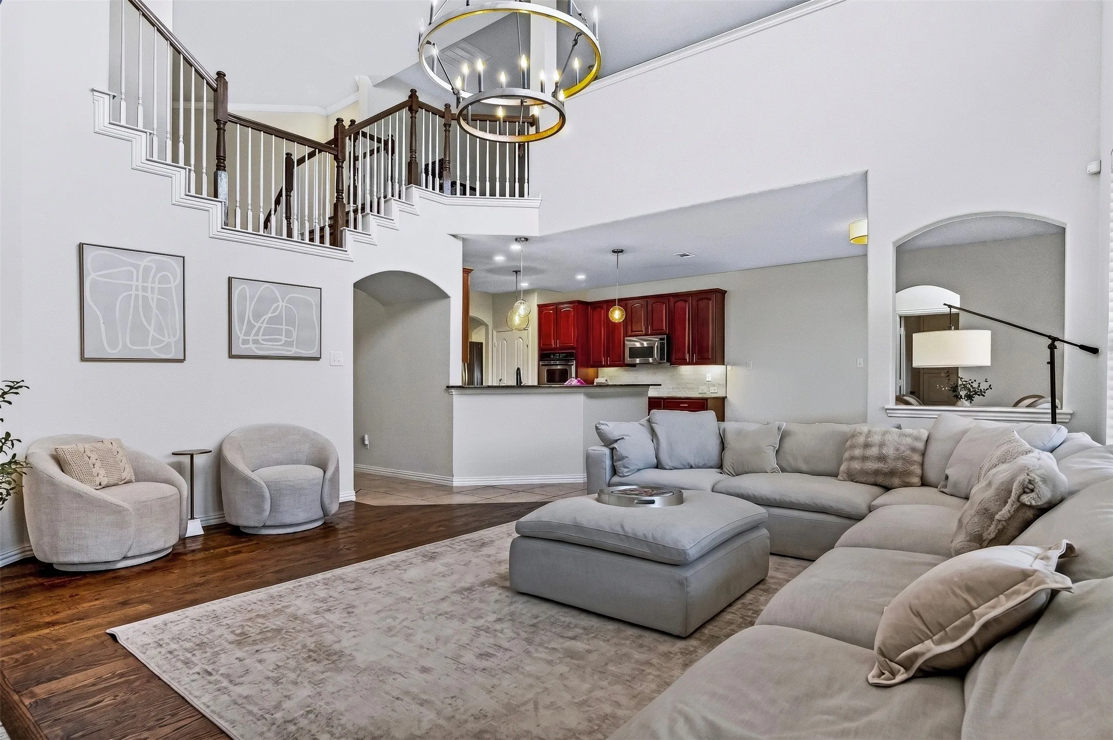 Two-story living area featuring wood-finish flooring, a grand staircase with dark wood railings, and a large chandelier