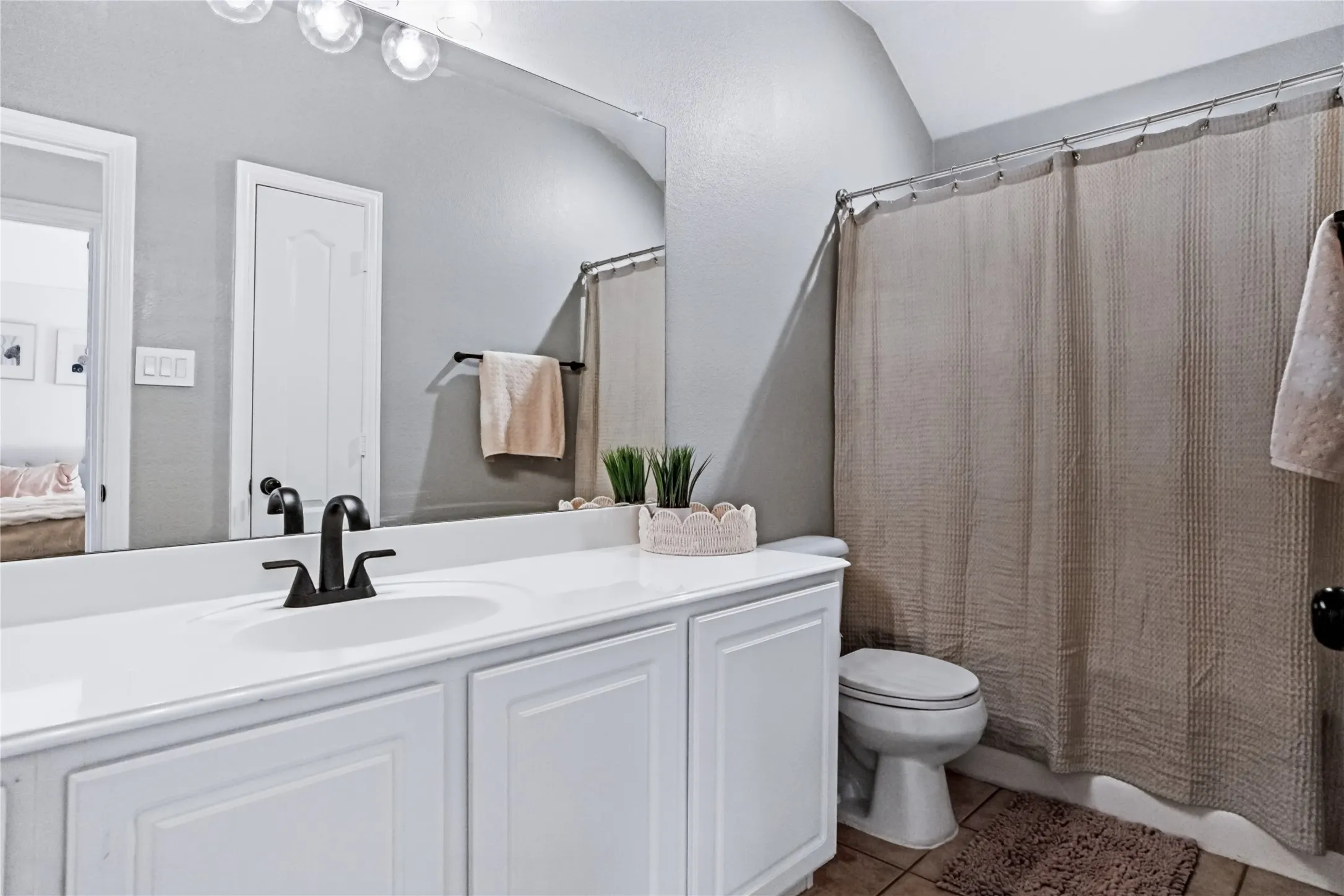White vanity with panel-front cabinetry, single basin sink, matte black faucet, and a large wall-mounted mirror