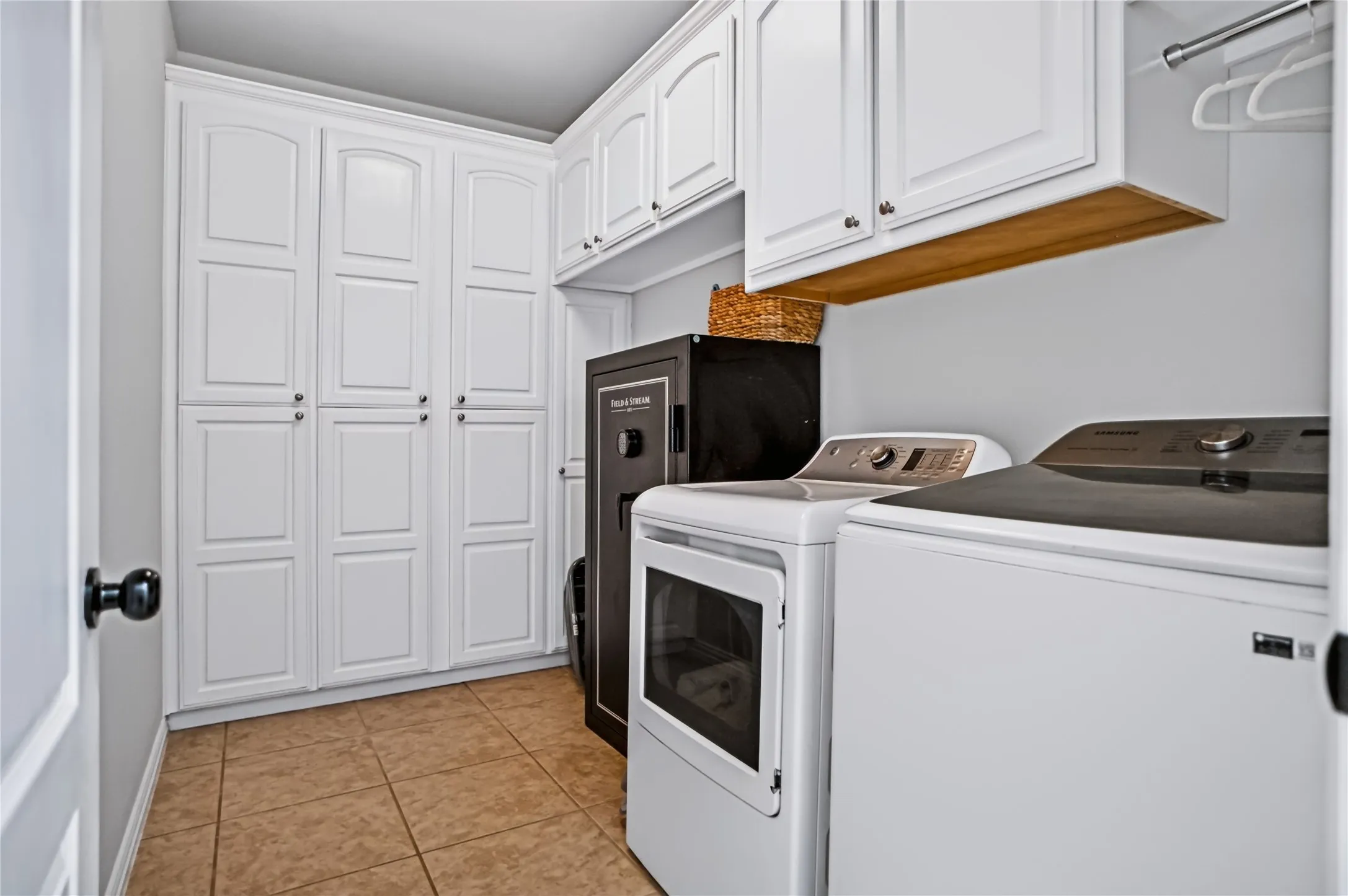 White paneled cabinetry, upper white cabinetry, light tile flooring, and a clothes hanging rod