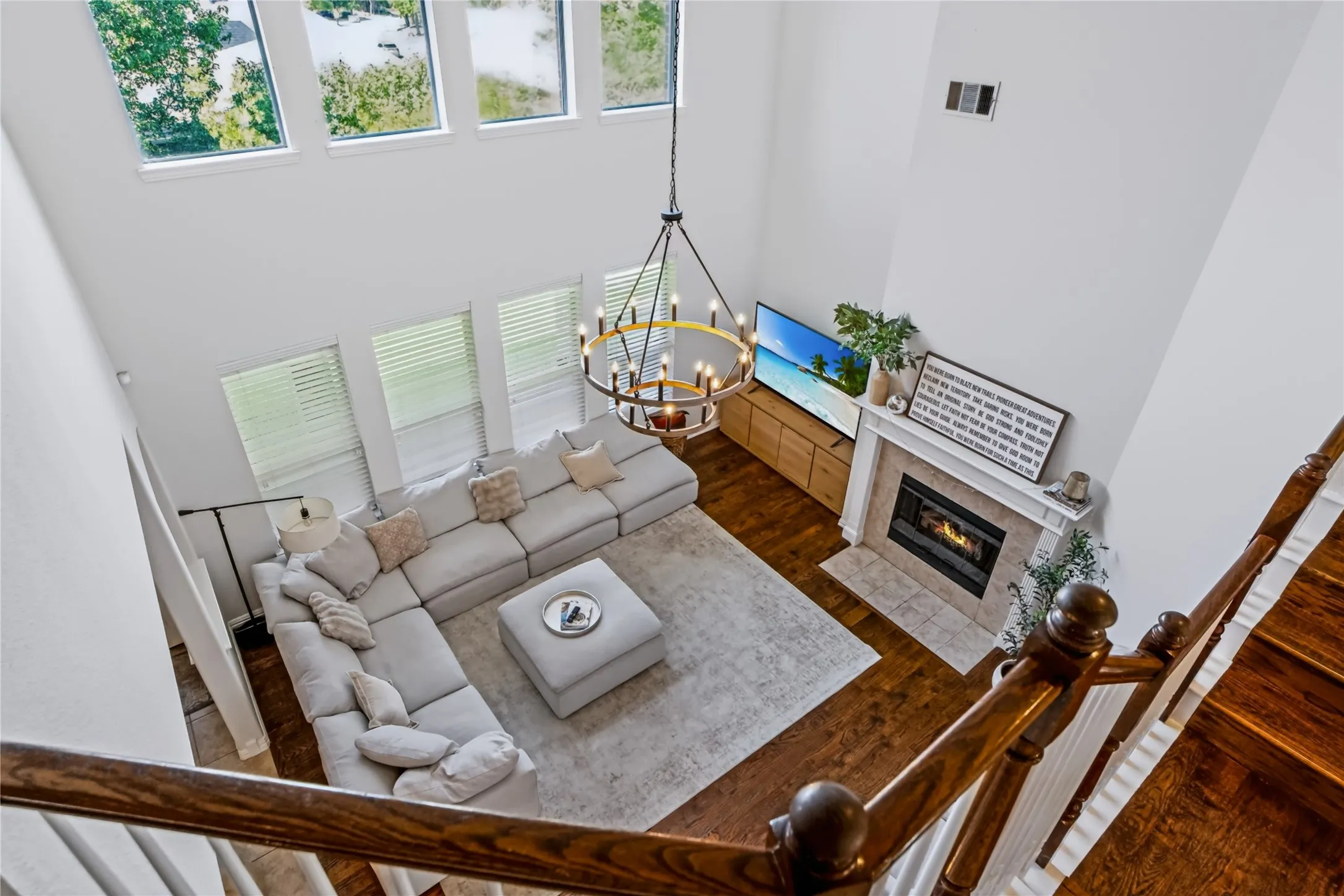 Two-story living area with high ceilings, multiple windows, a stone-tiled fireplace, and a decorative chandelier