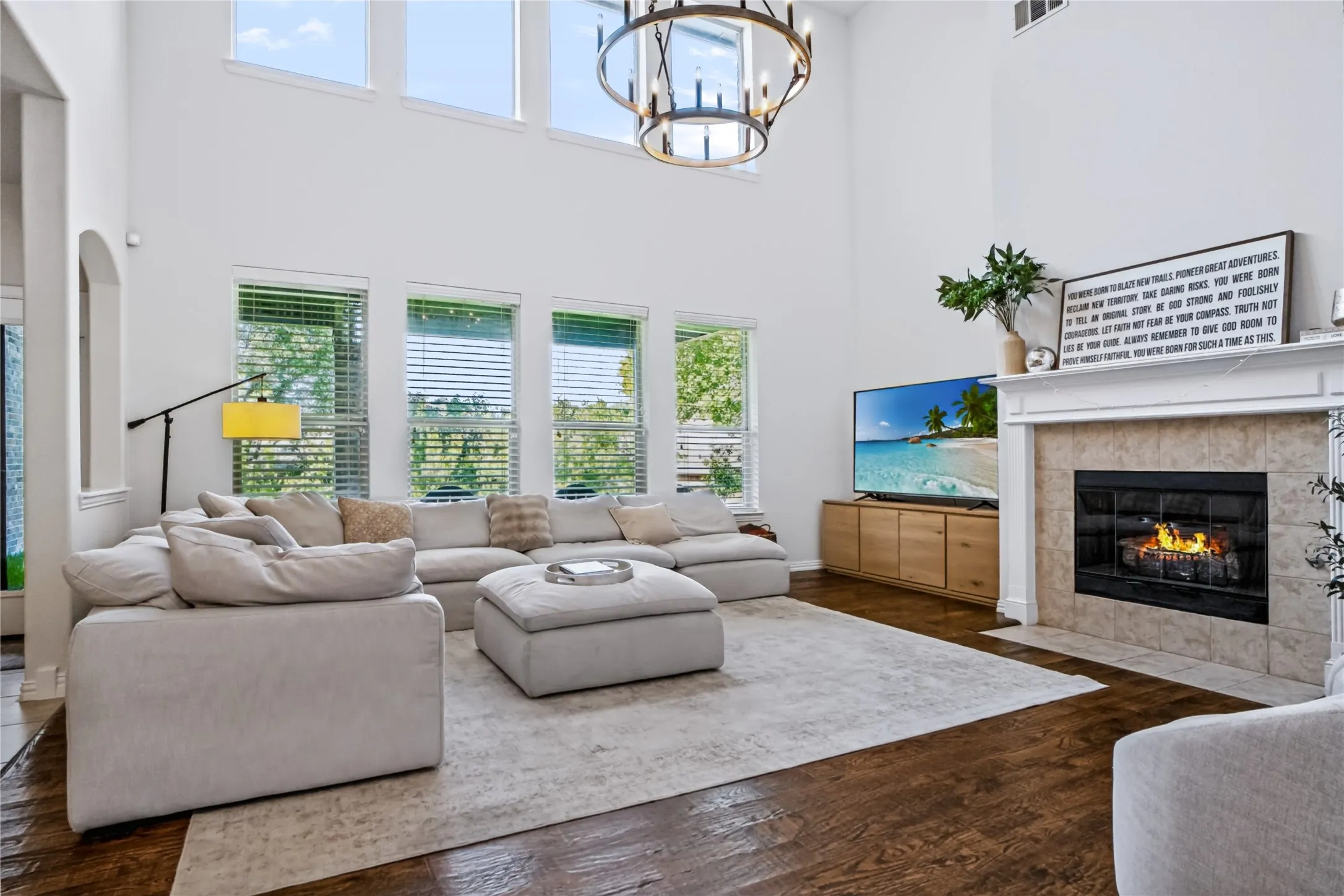 Two-story living area featuring a fireplace with a tile surround, tall windows, wood-finish flooring, and a chandelier
