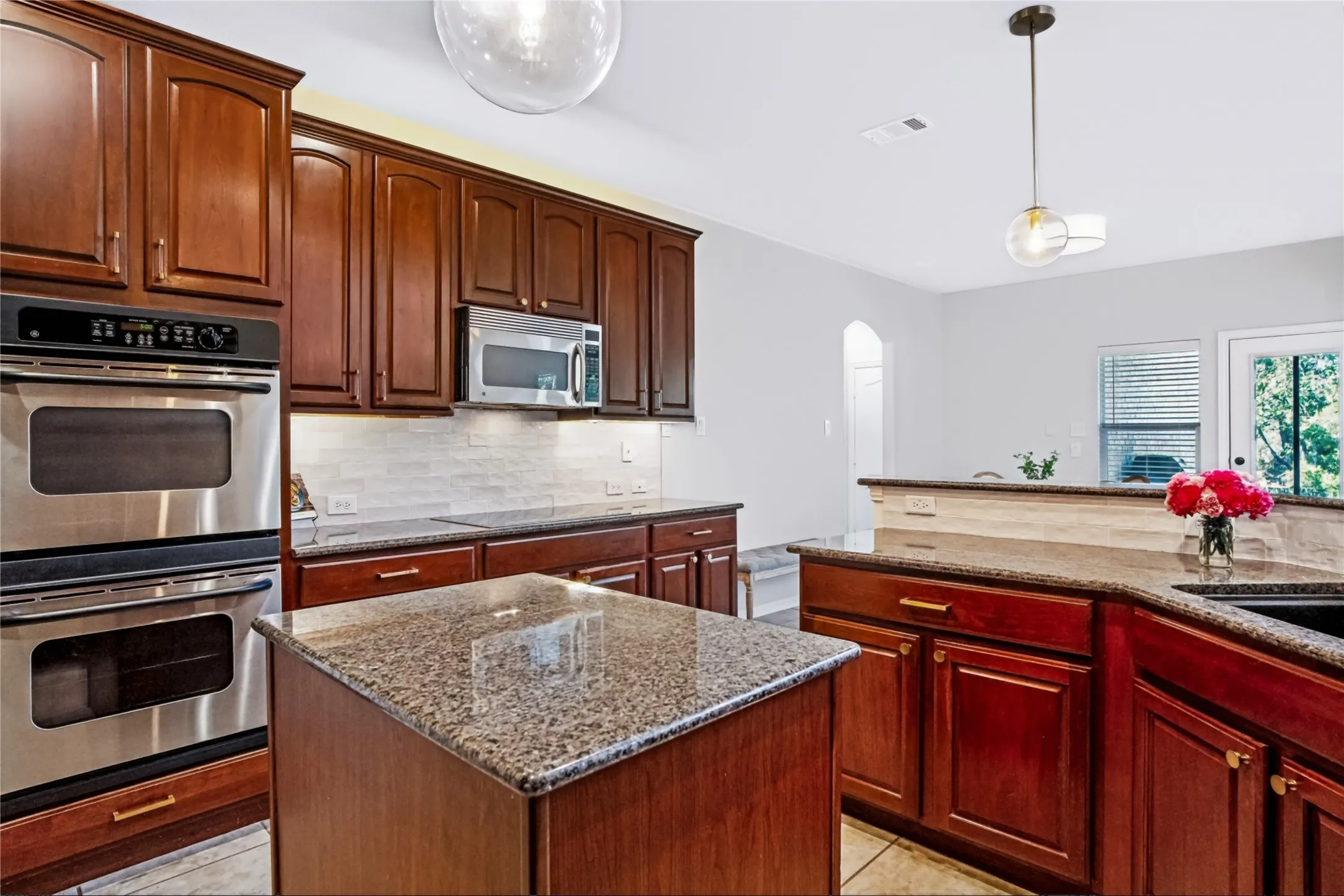 Kitchen featuring wood cabinetry, stainless steel double ovens, a center island with granite countertops, and a tile backsplash