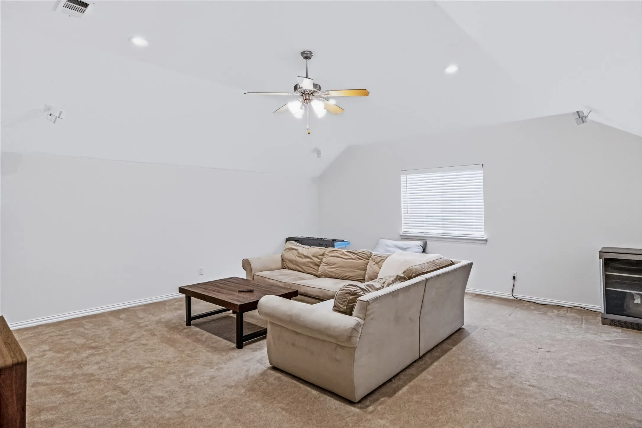 Spacious open-concept living area featuring vaulted ceilings with recessed lighting, a ceiling fan with integrated light fixture, and neutral carpet flooring