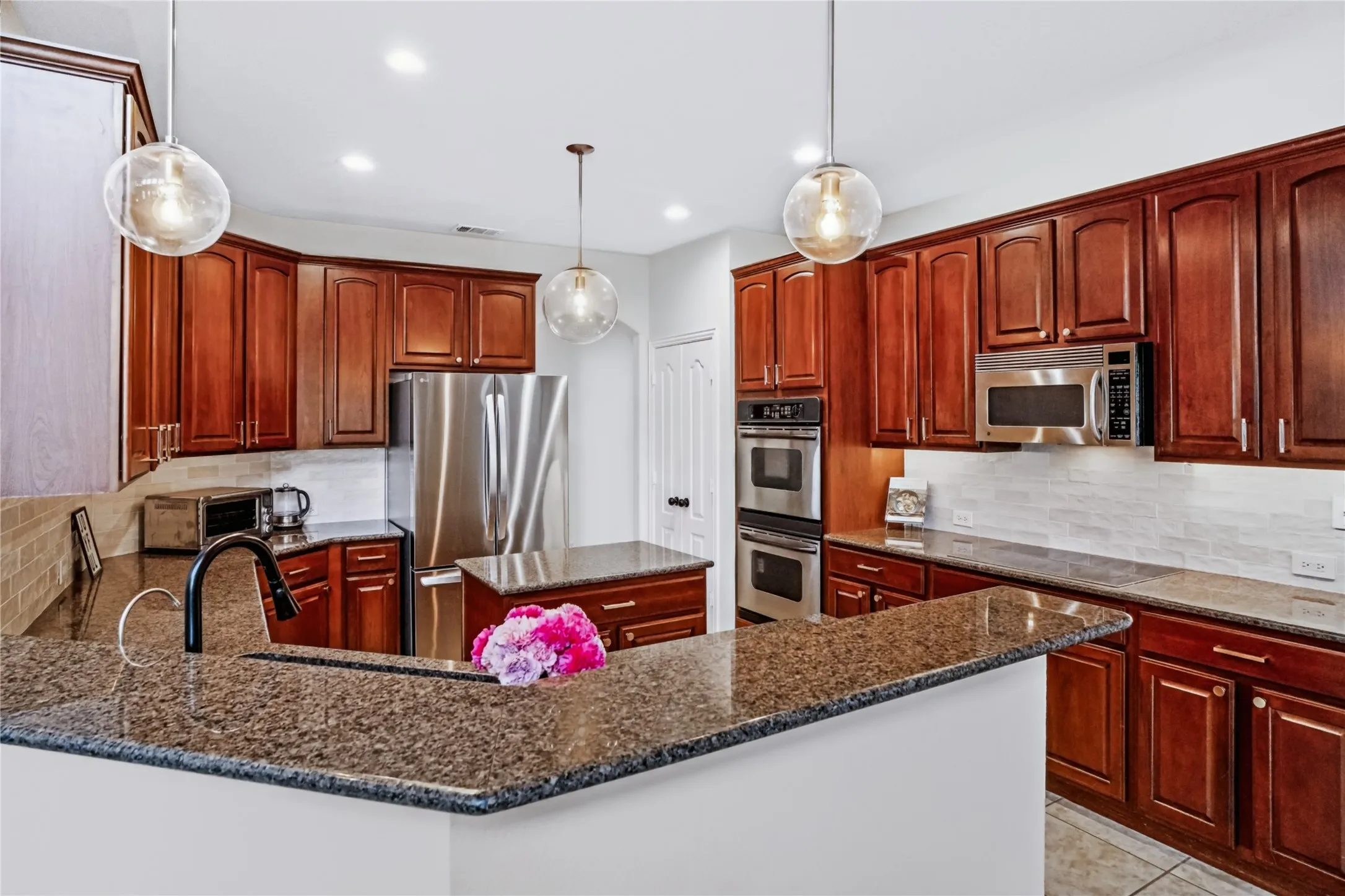 Chef's kitchen featuring rich wood cabinetry, granite countertops, stainless steel appliances including double wall ovens, and a generous center island with seating