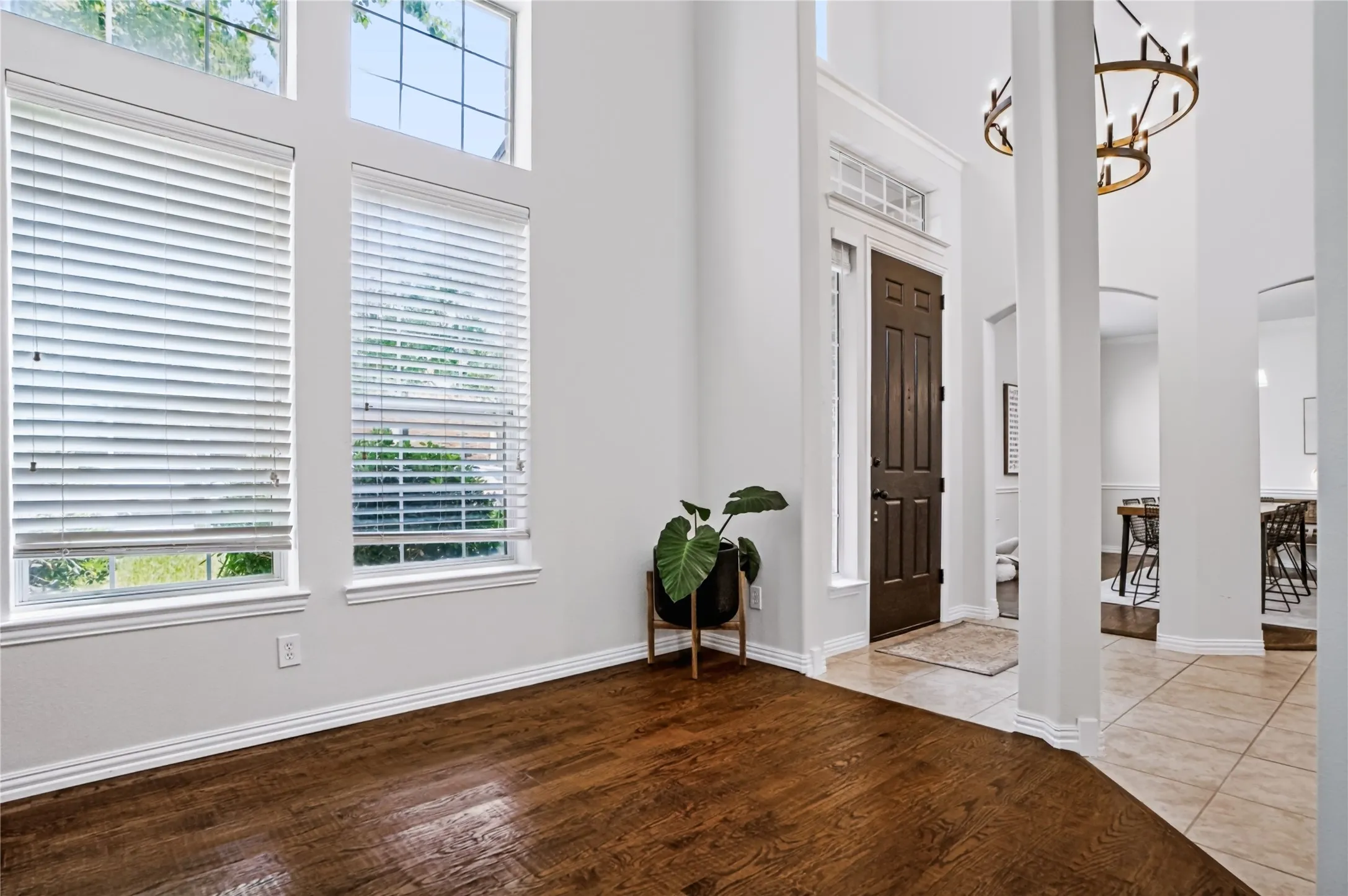 Entryway featuring high ceilings, a dark wood-paneled door, tall windows with white blinds, and wood-finish flooring