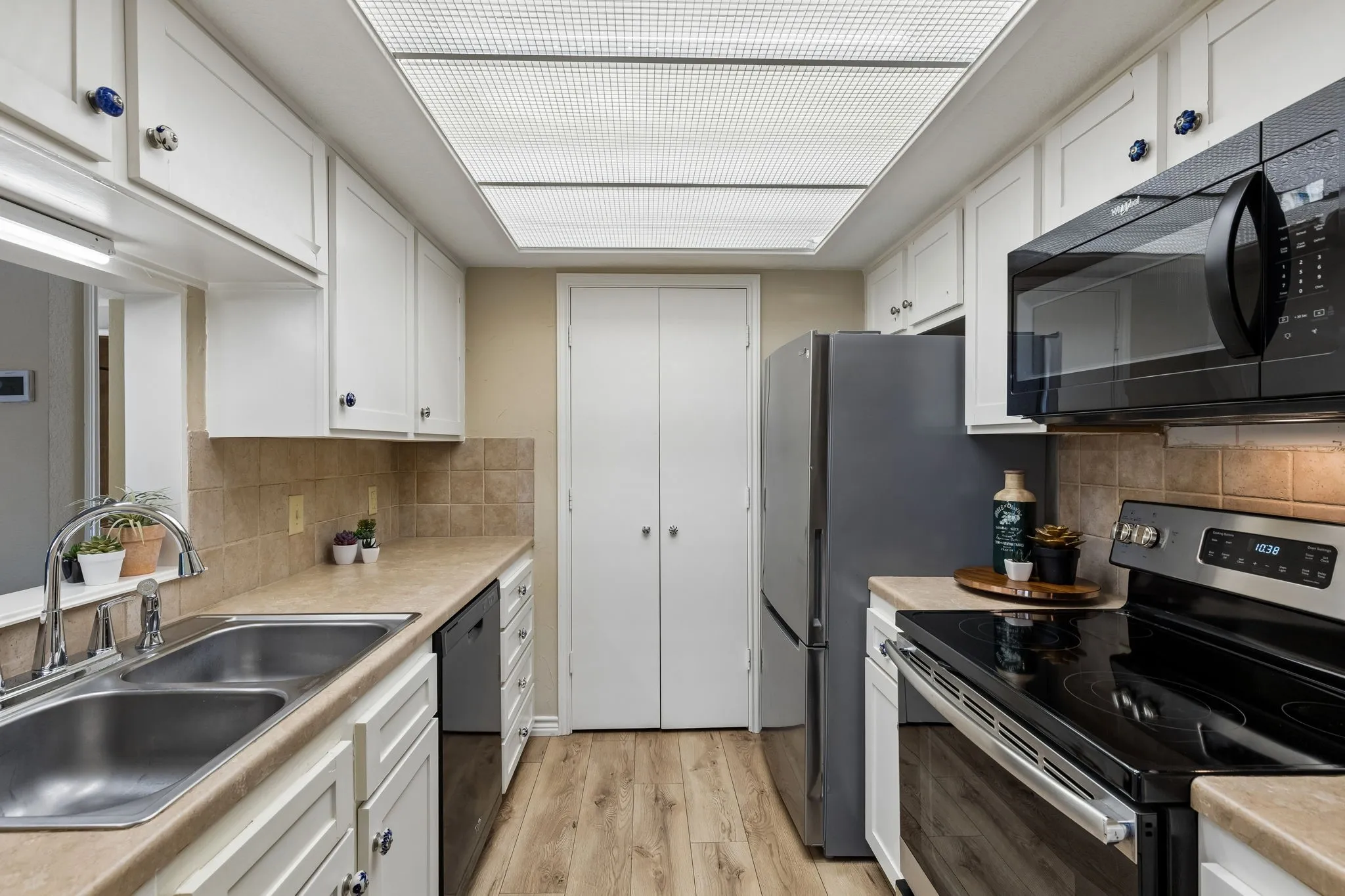 Galley kitchen featuring white cabinetry, stainless steel appliances and neutral tile backsplash