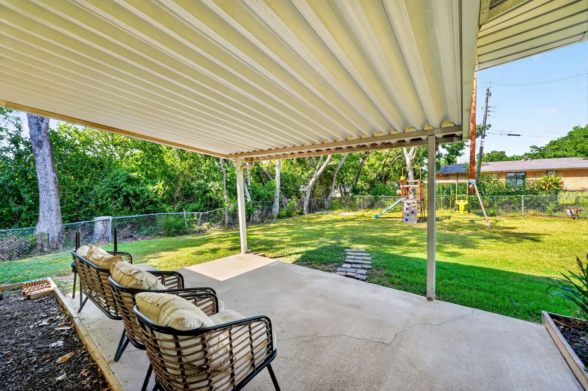 Expansive covered patio with louvered aluminum pergola roof system and concrete flooring, overlooking manicured lawn and mature shade trees