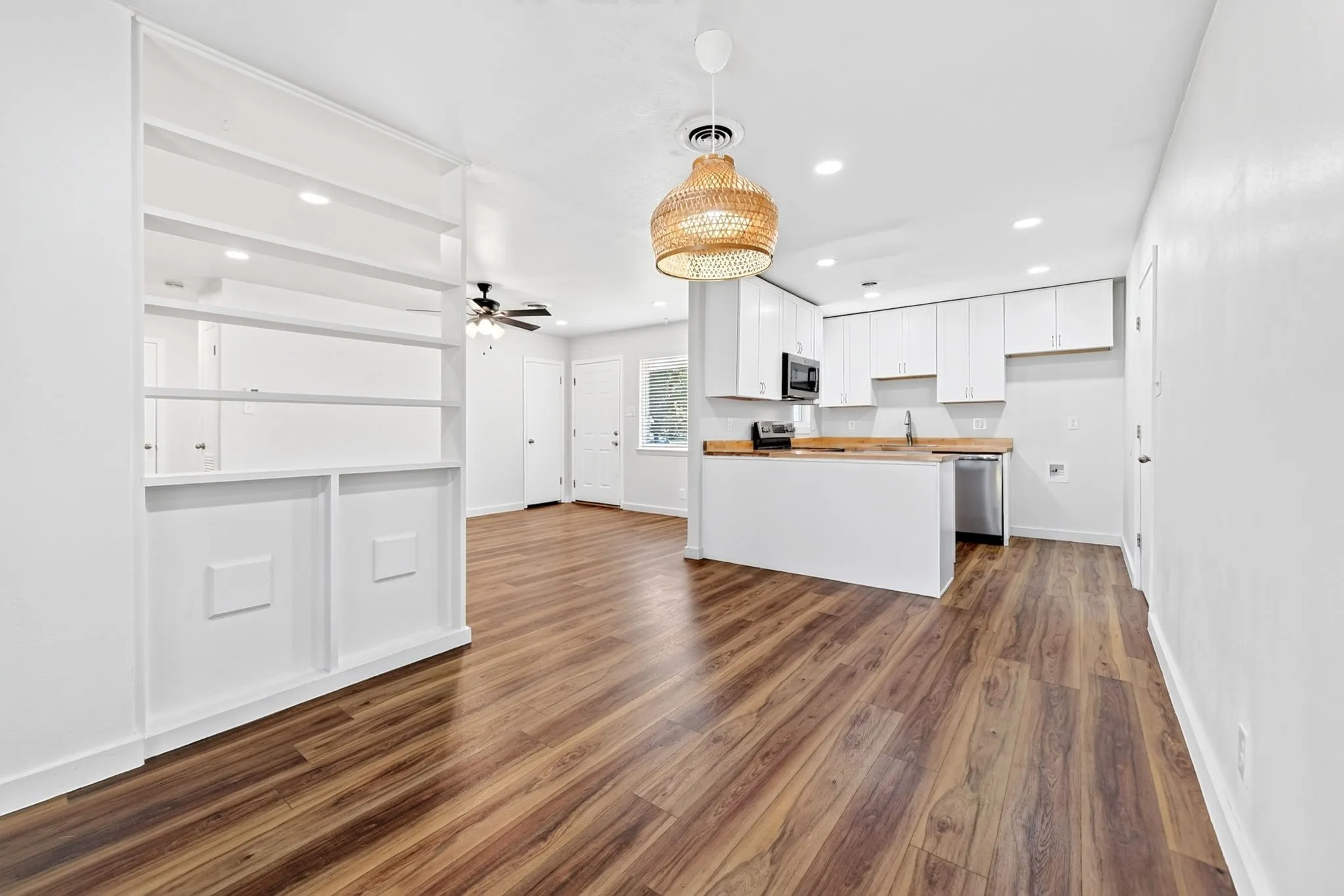 Wood-finish flooring throughout, with a built-in shelving unit, white cabinetry, and wood-finish countertops