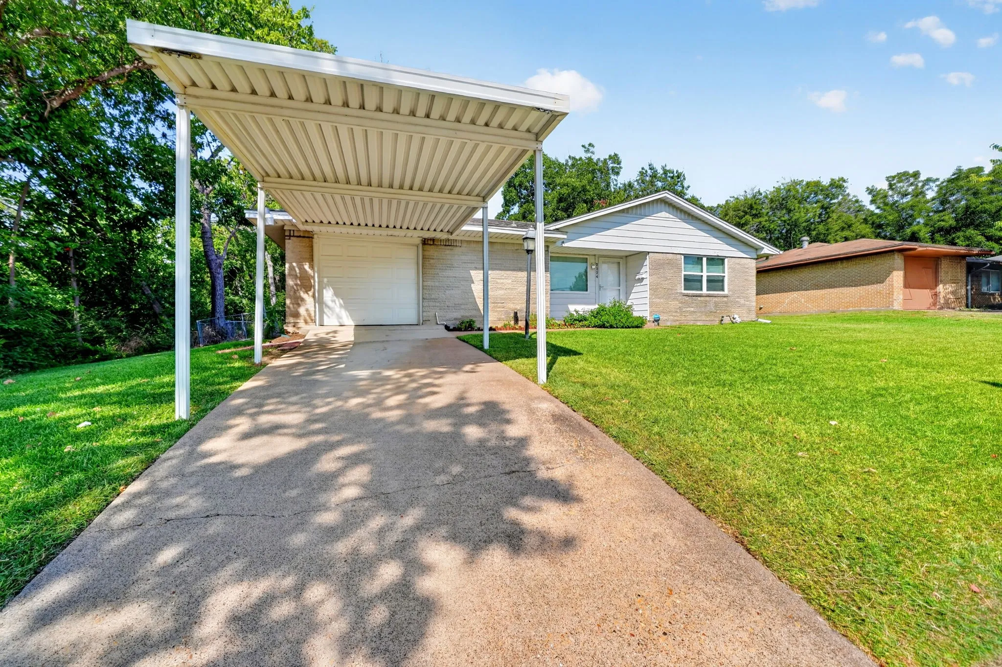 Exterior featuring a carport, concrete driveway, attached garage, and a brick and siding facade