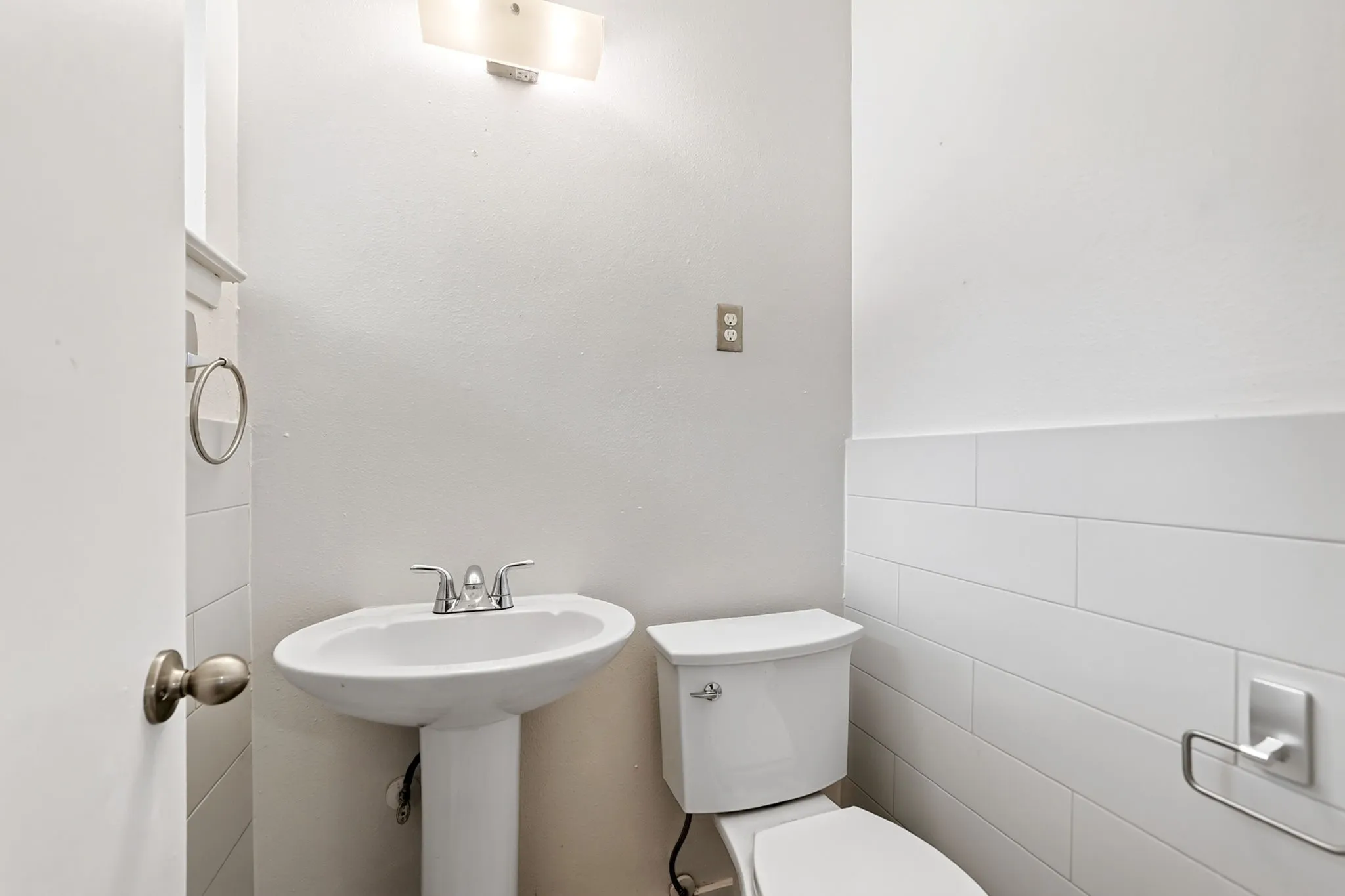 Pedestal sink with chrome faucet, toilet, wall-mounted light fixture, and white wall tiling