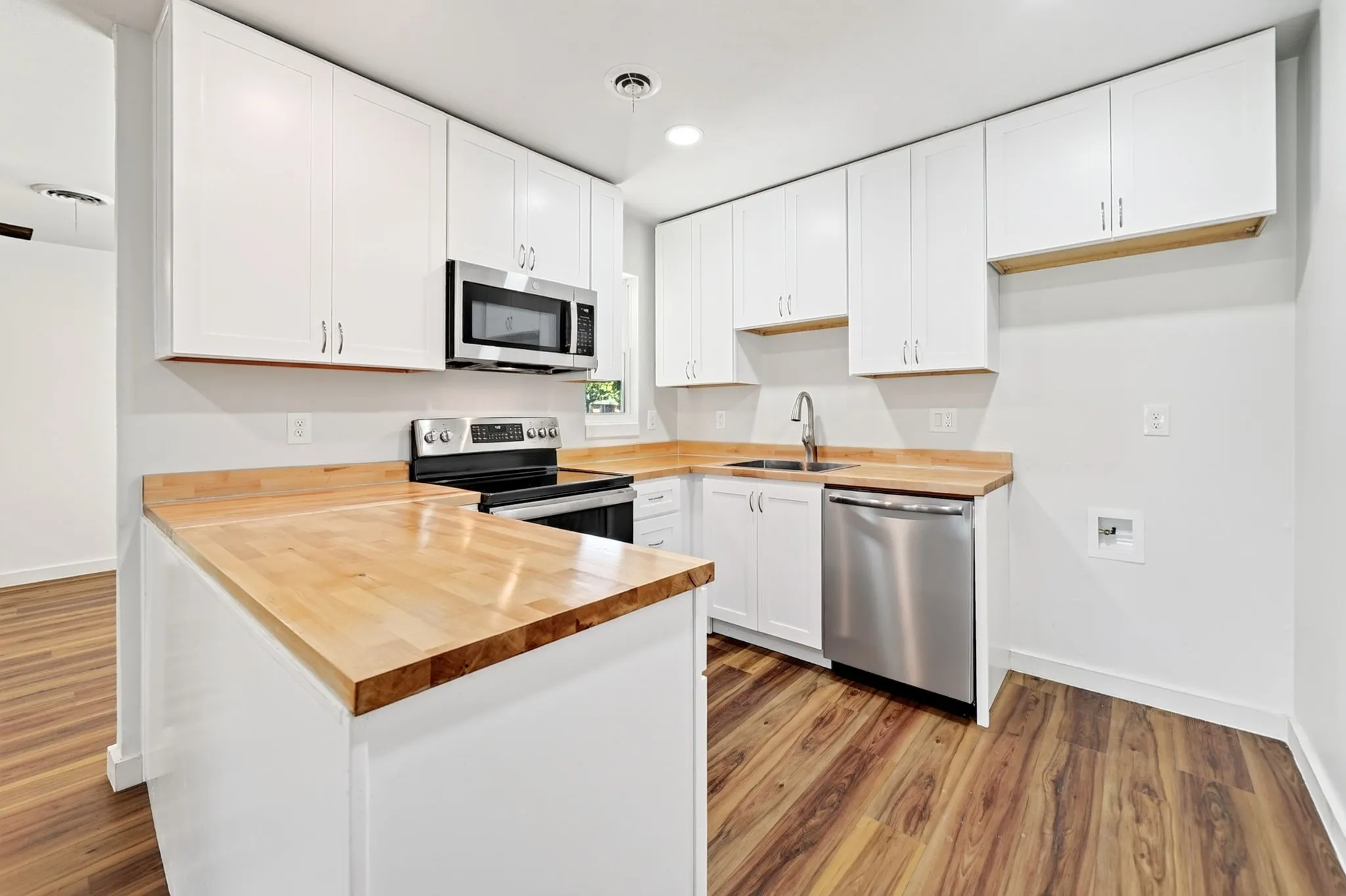 Kitchen featuring white cabinetry, wood-finish countertops, stainless steel appliances, and wood-finish flooring