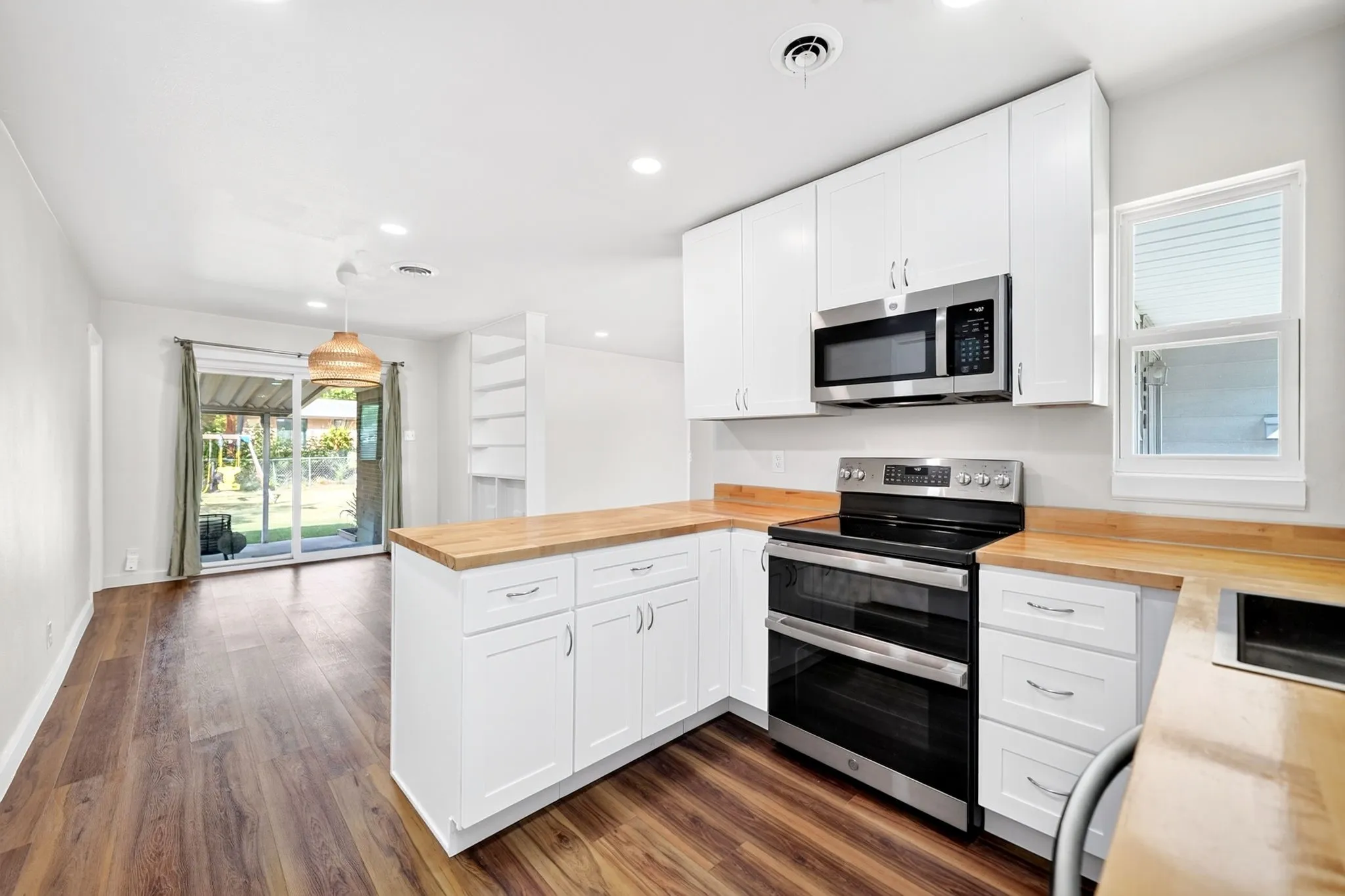 Open-concept kitchen featuring wood-finish flooring, white cabinetry, stainless steel appliances, and a wood-finish countertop