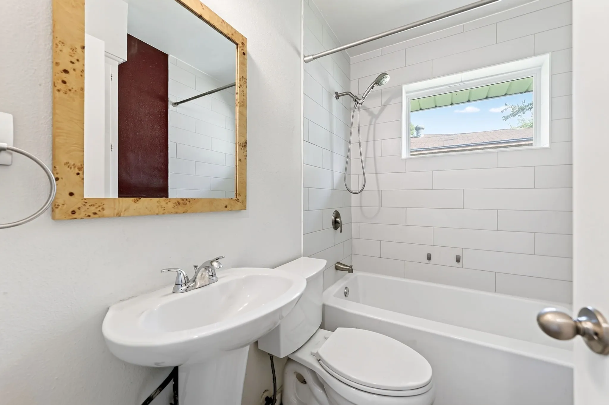Pedestal sink with chrome fixtures, white subway tile shower surround, shower/tub combination, and a framed wall mirror