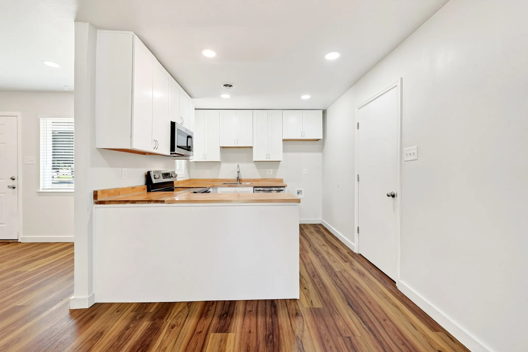 Kitchen featuring white cabinetry, wood-finish countertops, stainless steel appliances, and wood-finish flooring