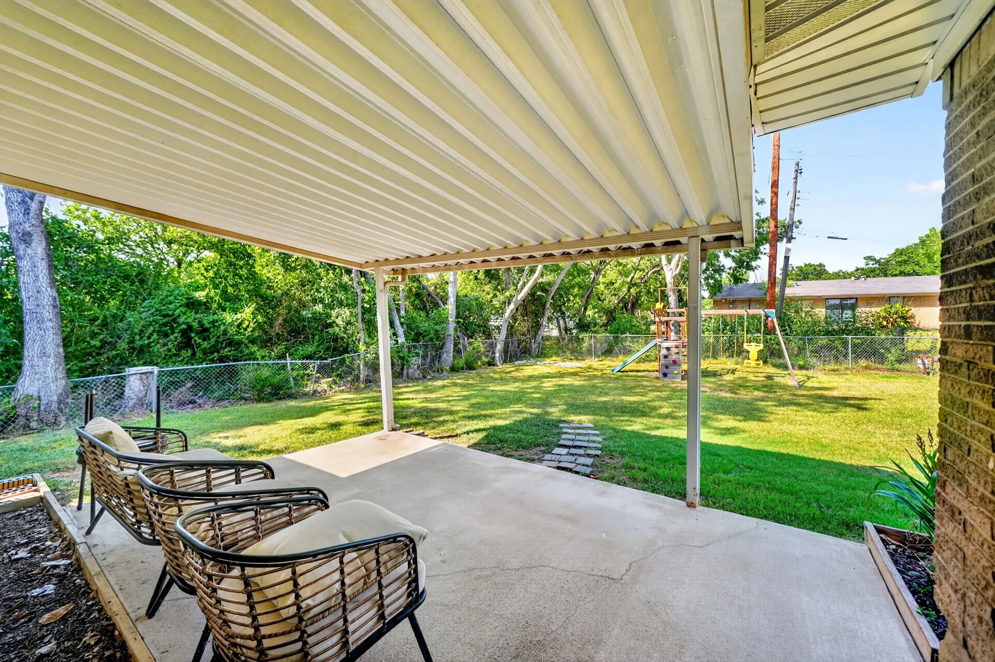 Covered concrete patio with a lush green lawn and mature trees