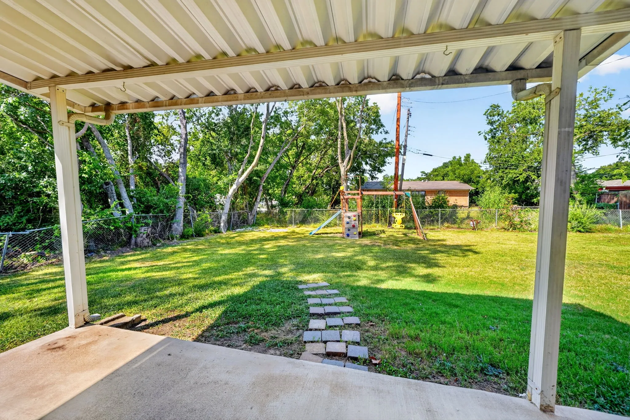 Covered patio with concrete flooring, leading to a lawn with a stone pathway