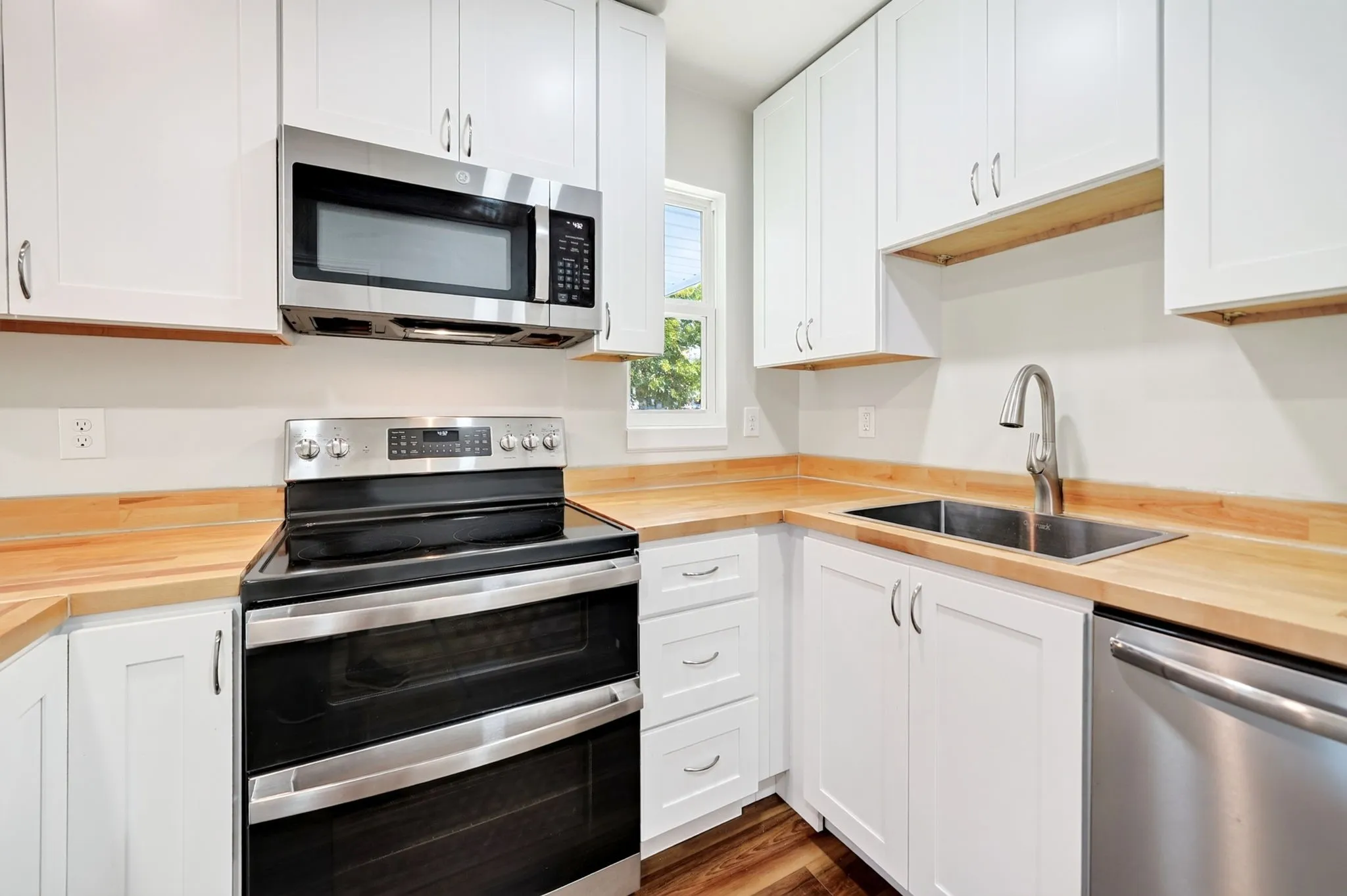 White shaker cabinetry, wood-finish countertops, stainless steel appliances, double basin kitchen sink, and wood-finish flooring